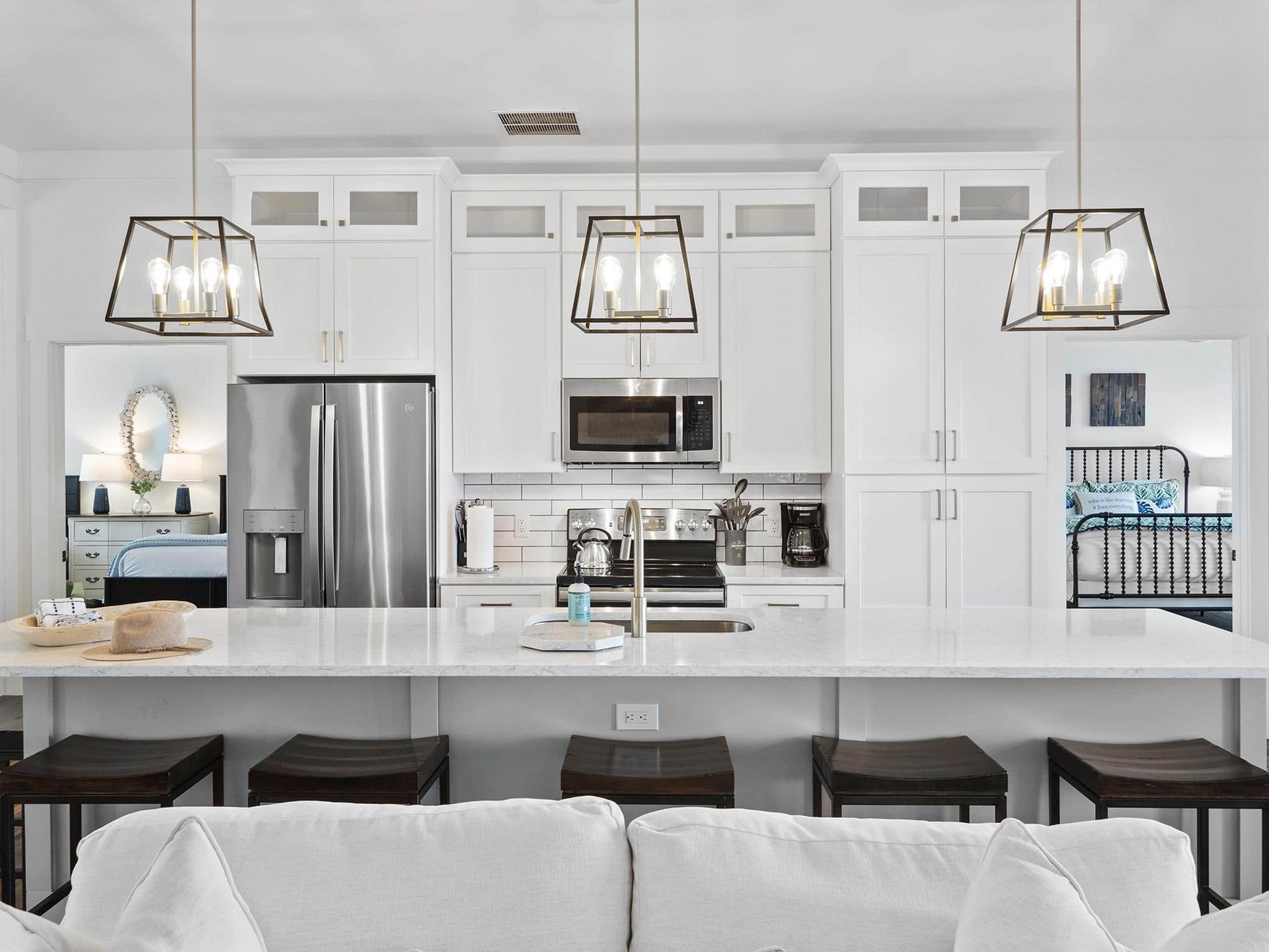 A kitchen with white cabinets , a stainless steel refrigerator , a microwave , and a couch.