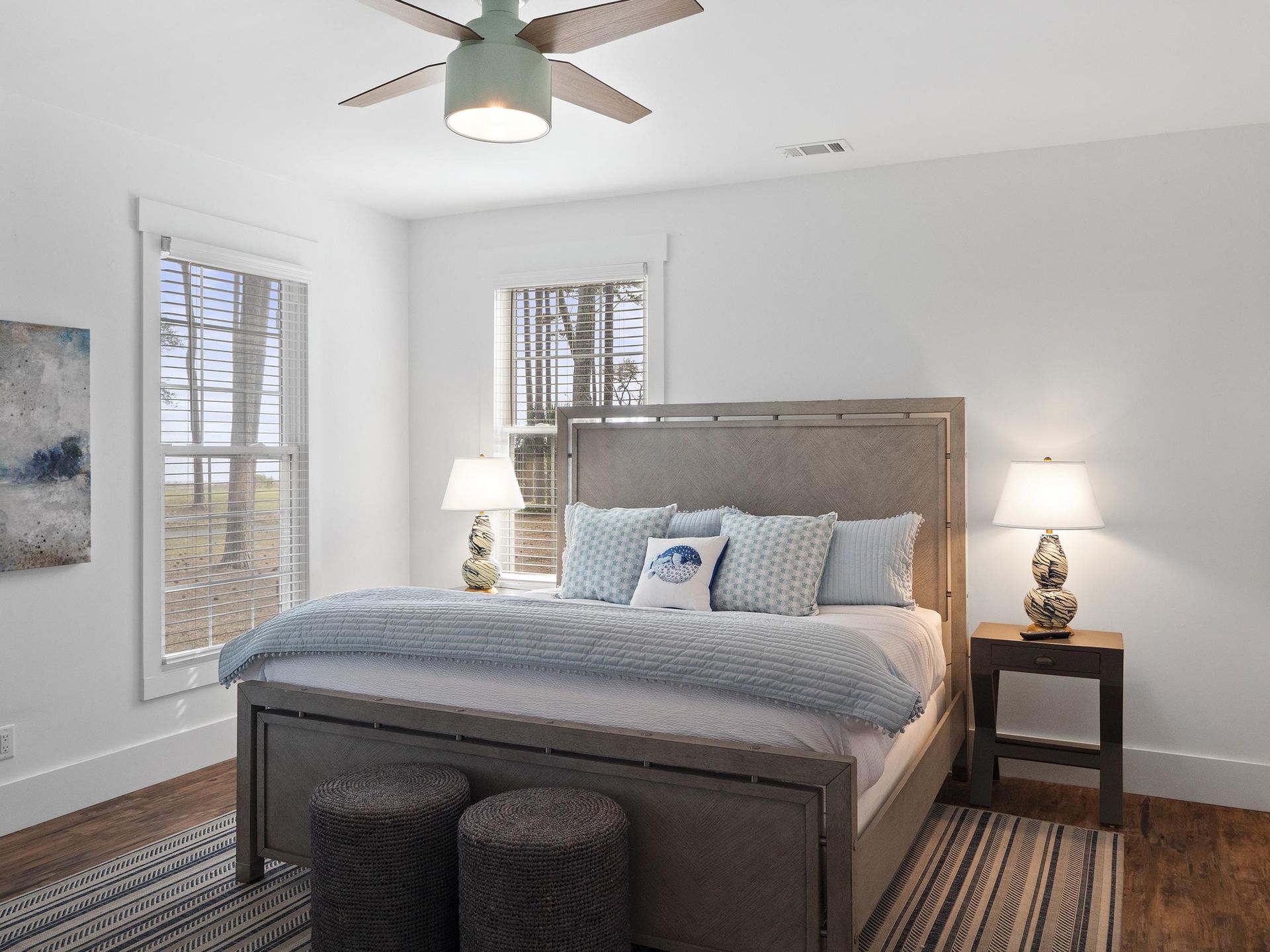 A bedroom with a king size bed , two lamps , a nightstand , and a ceiling fan.