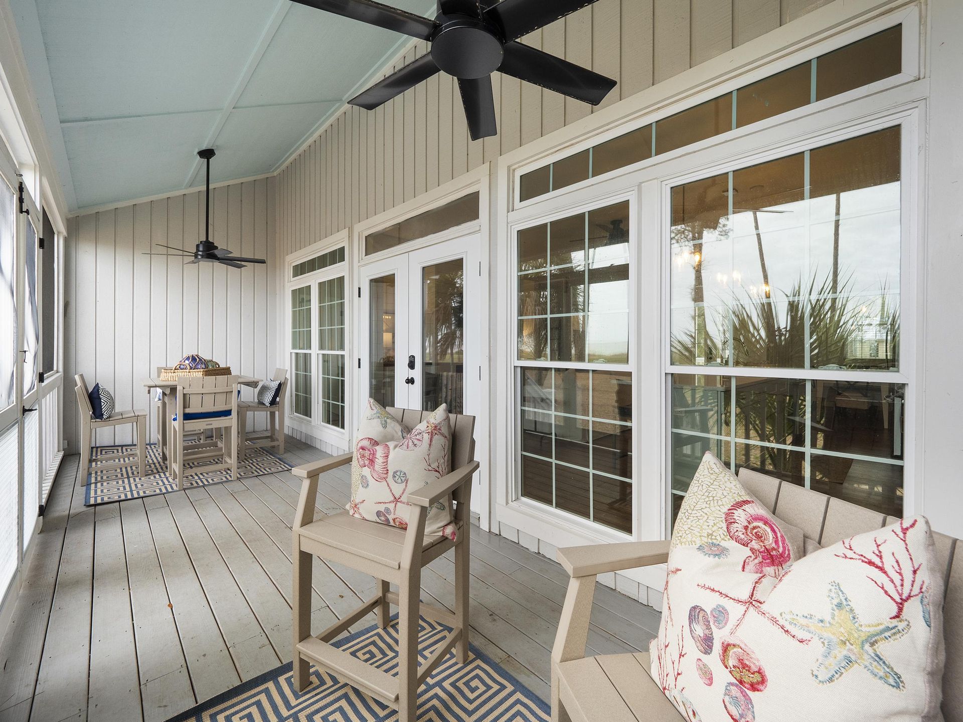 A screened in porch with a table and chairs and a ceiling fan.