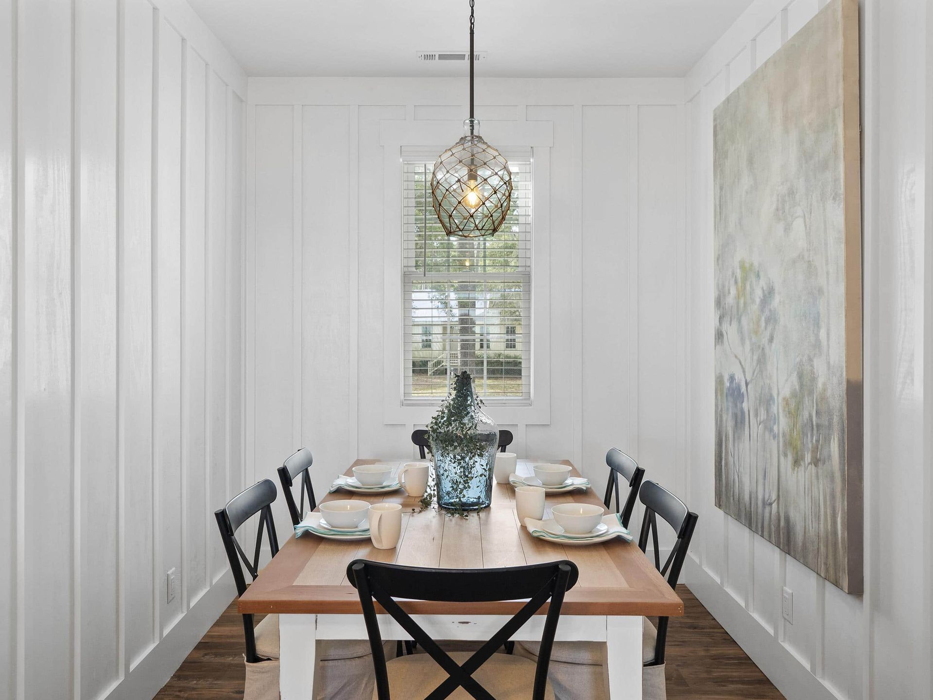 A dining room with a table and chairs and a painting on the wall.