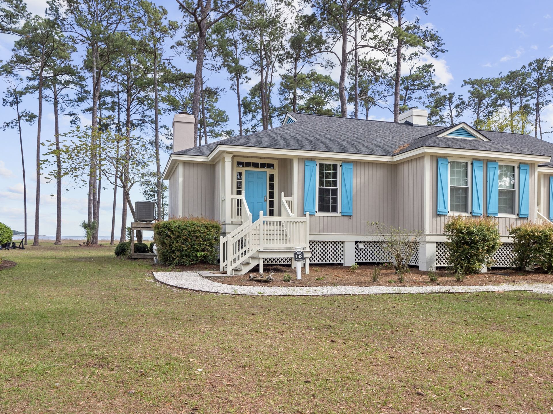 A small house with blue shutters on the windows is surrounded by trees.