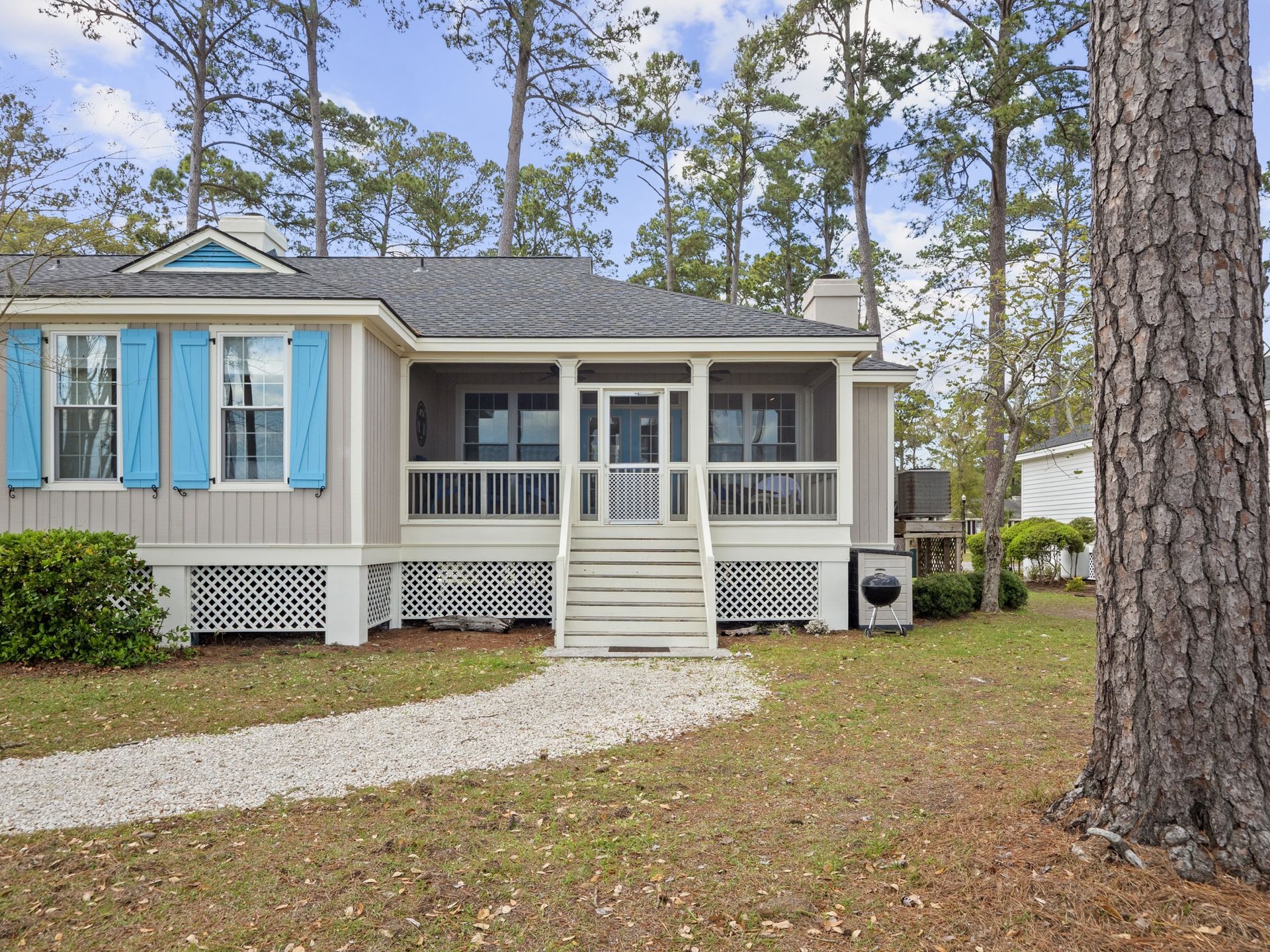 A mobile home with blue shutters and a porch surrounded by trees.