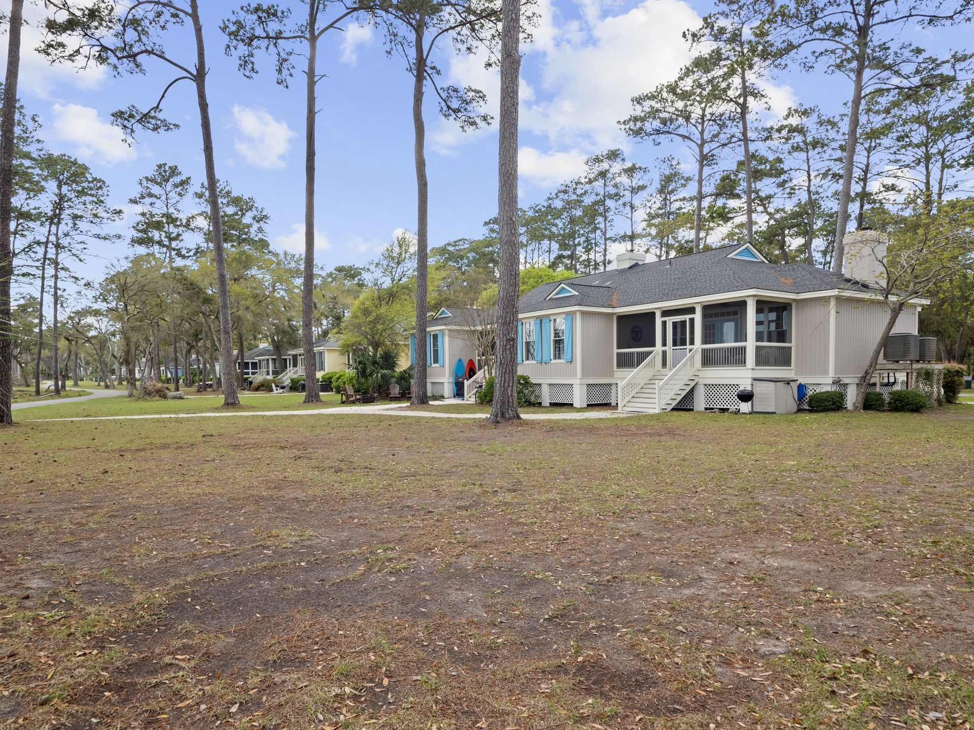 A white house with a screened in porch is surrounded by trees.
