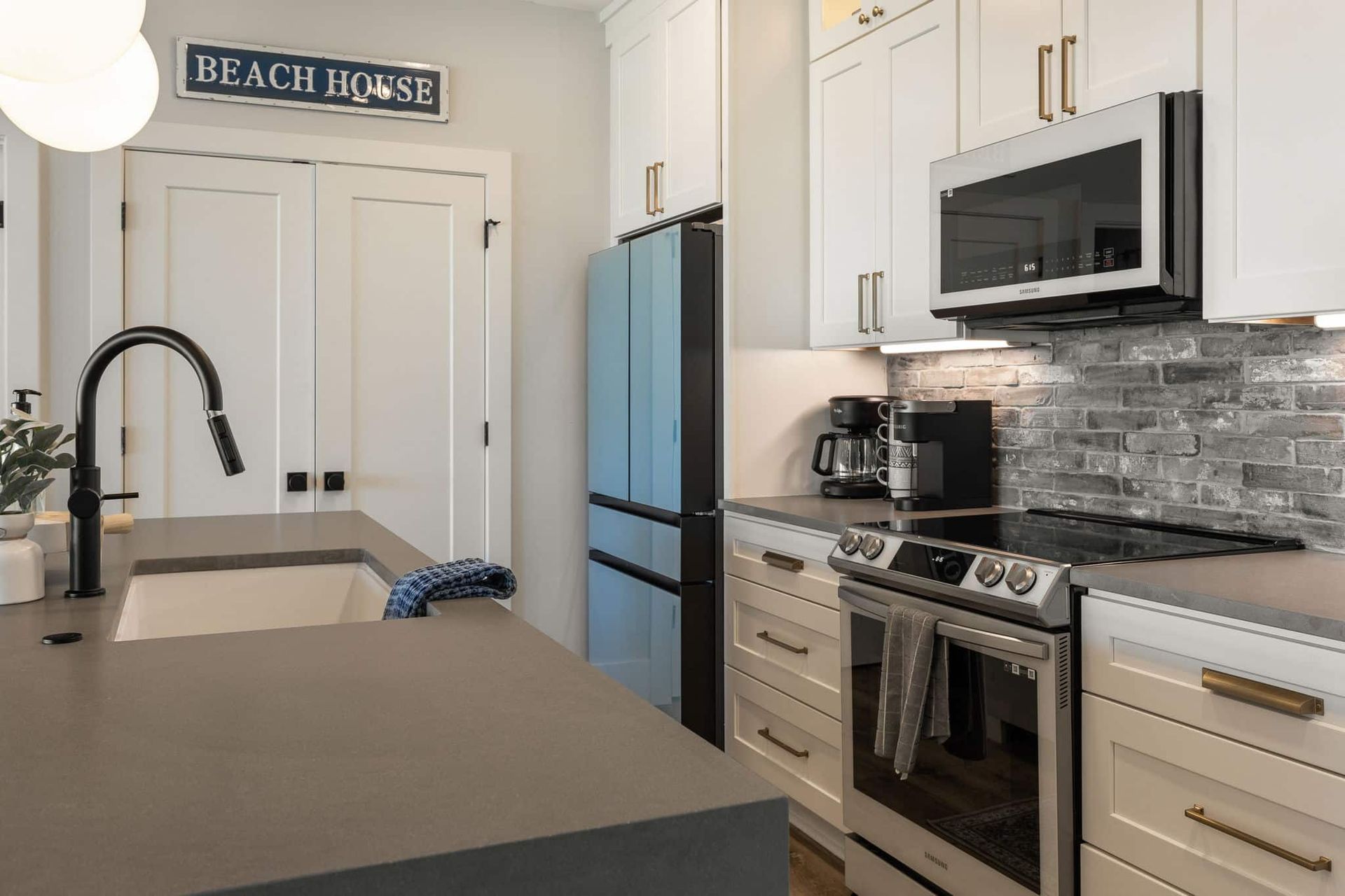 A kitchen with white cabinets , stainless steel appliances , a blue refrigerator and a sign that says beach house.