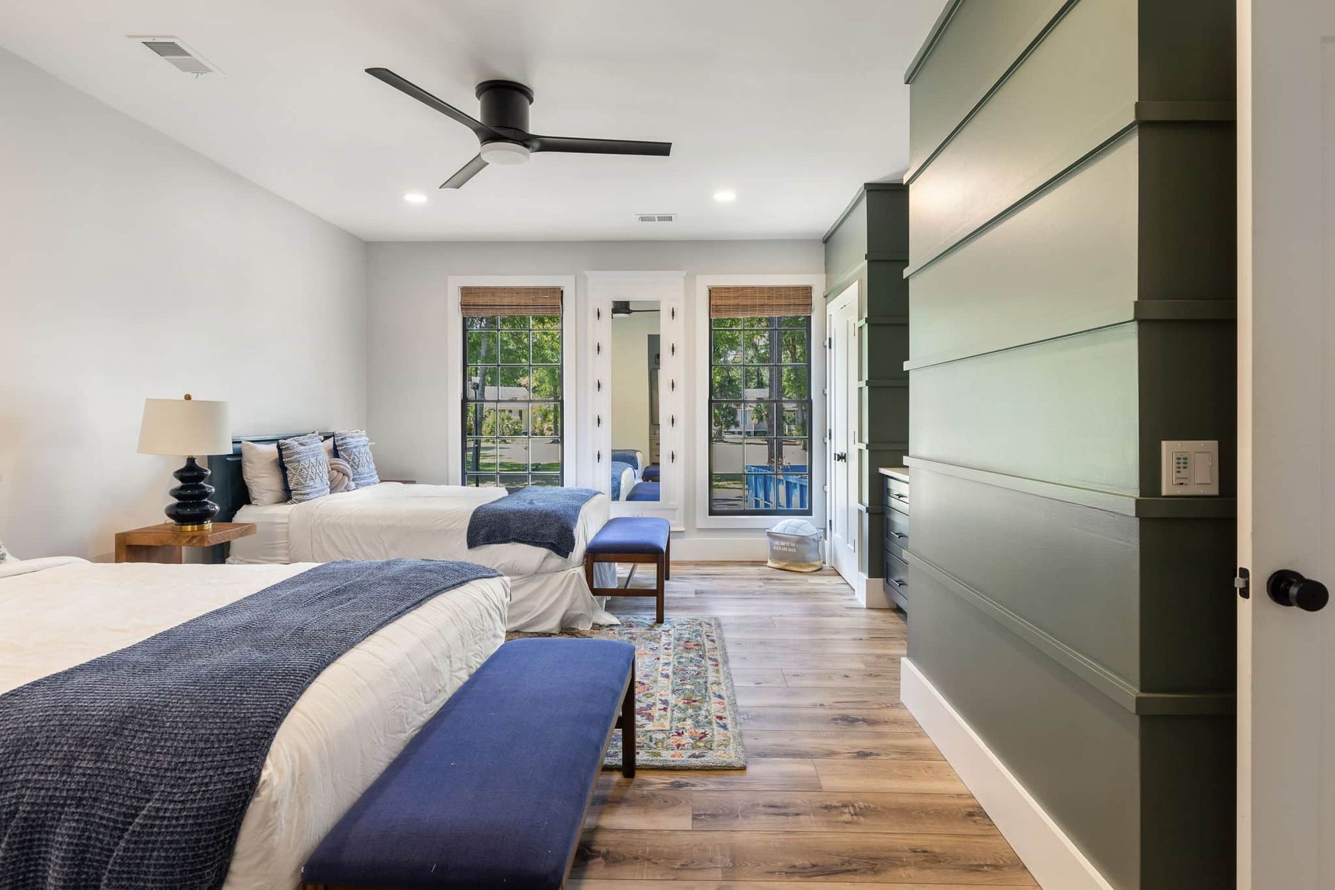 A bedroom with two beds , a bench and a ceiling fan.