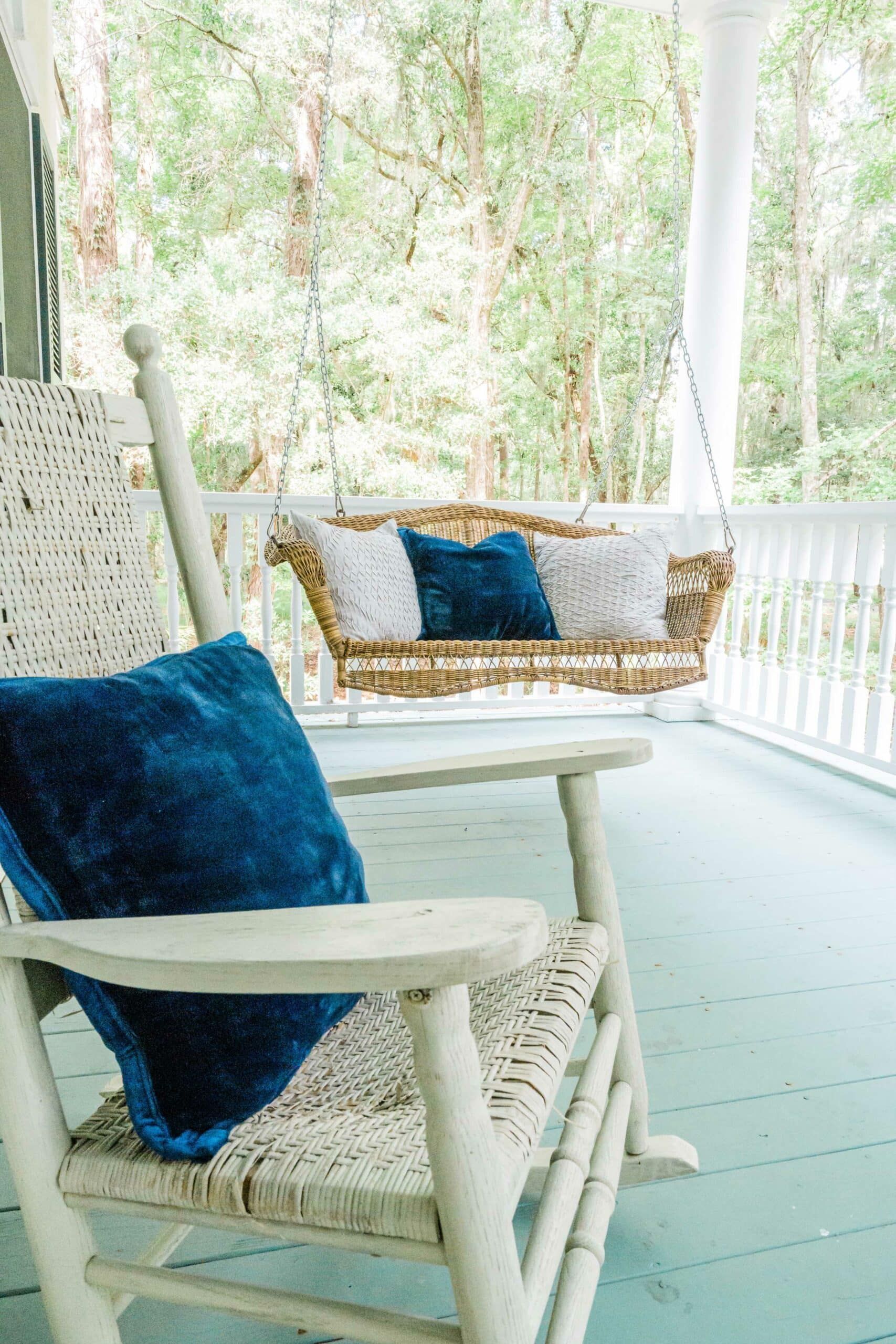 A white rocking chair with a blue pillow on it is on a porch next to a swing.