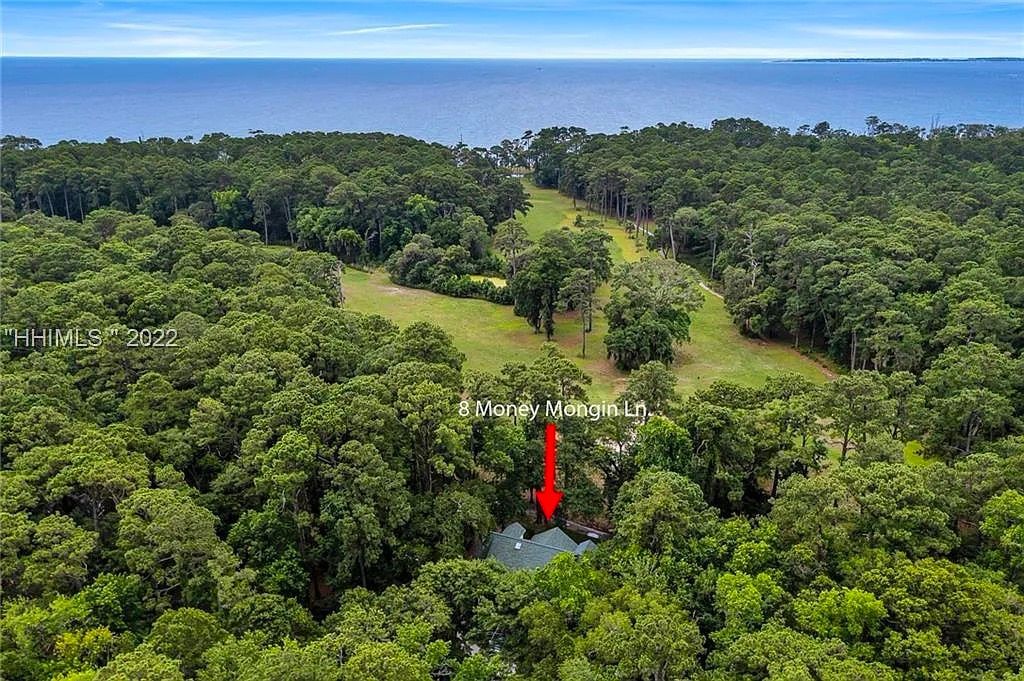 An aerial view of a house in the middle of a forest with a red arrow pointing to it.