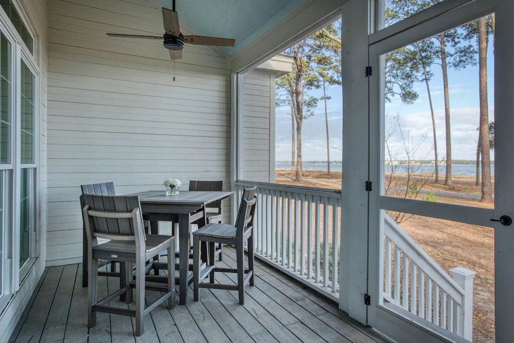 A screened in porch with a table and chairs and a ceiling fan.