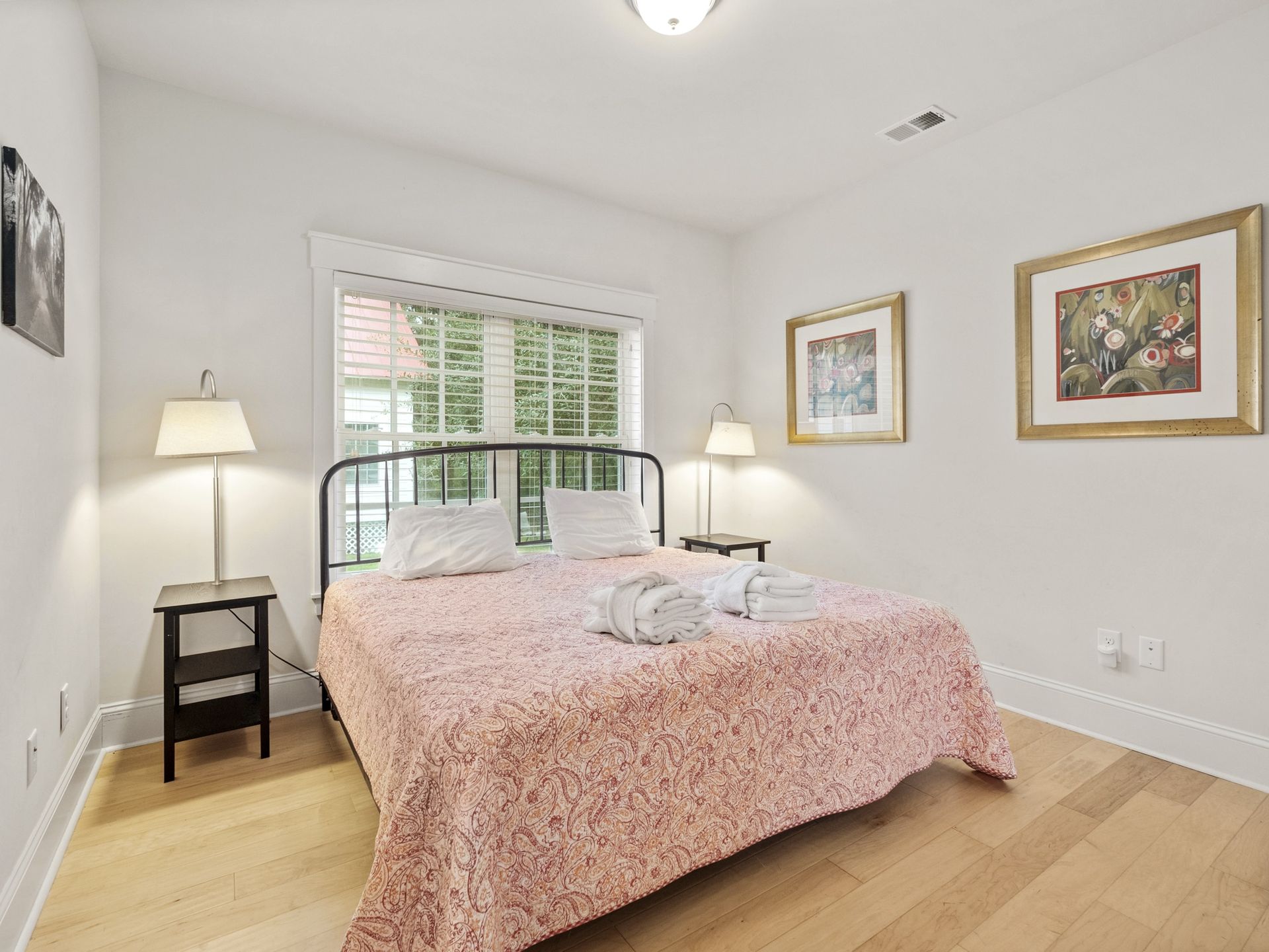 A bedroom with a bed , two nightstands , two lamps and two pictures on the wall.