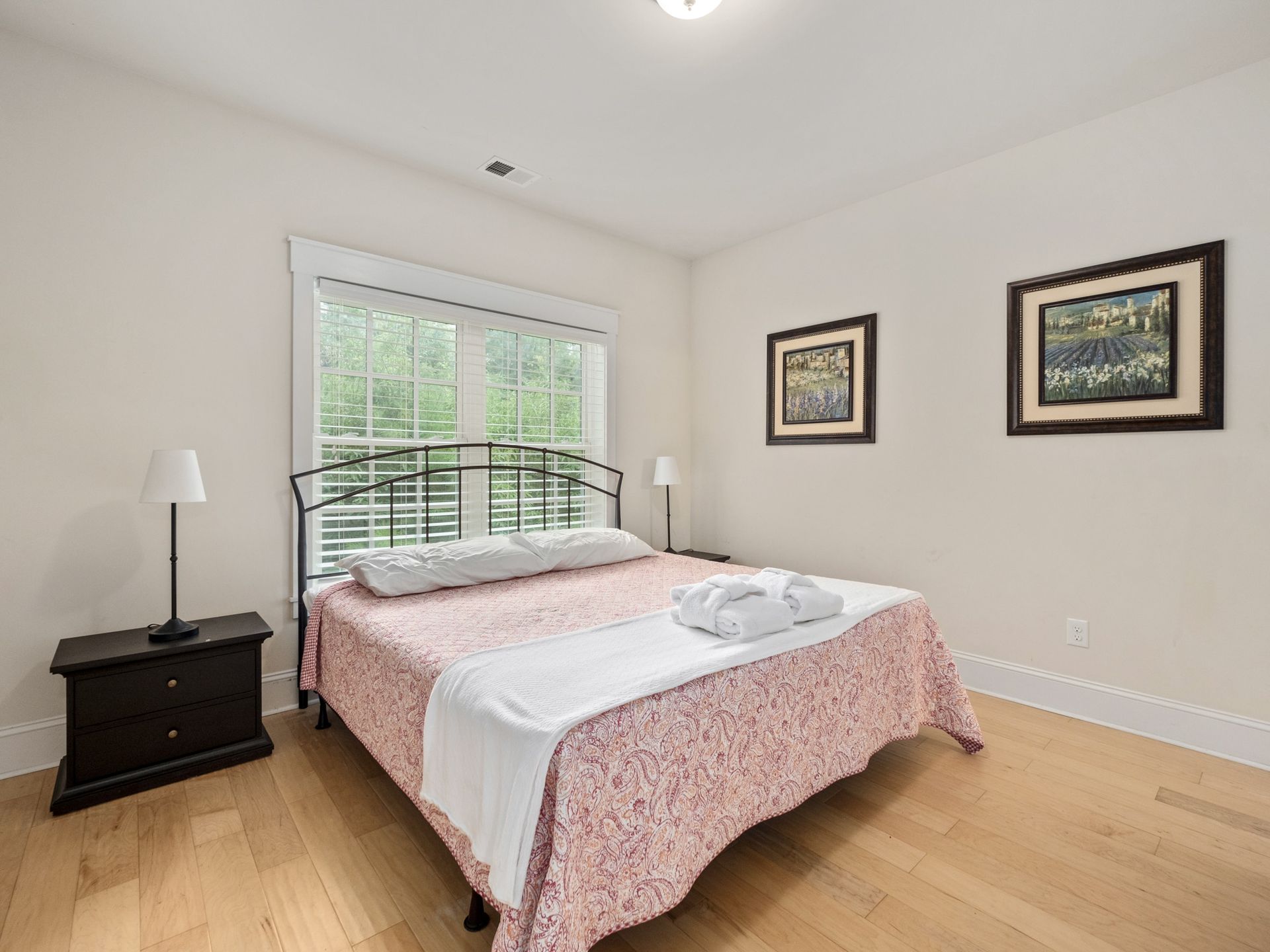 A bedroom with a king size bed , nightstand , and two paintings on the wall.