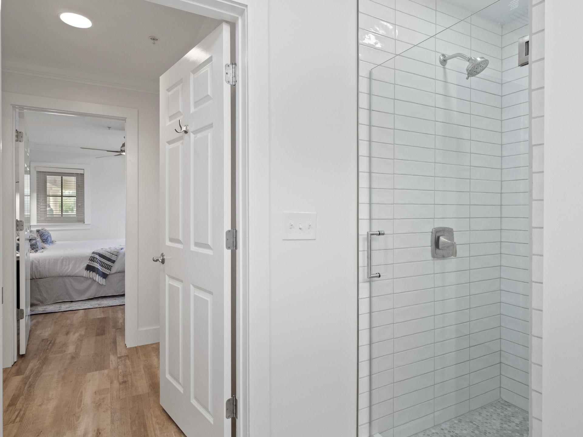 A bathroom with a walk in shower and a bedroom in the background.