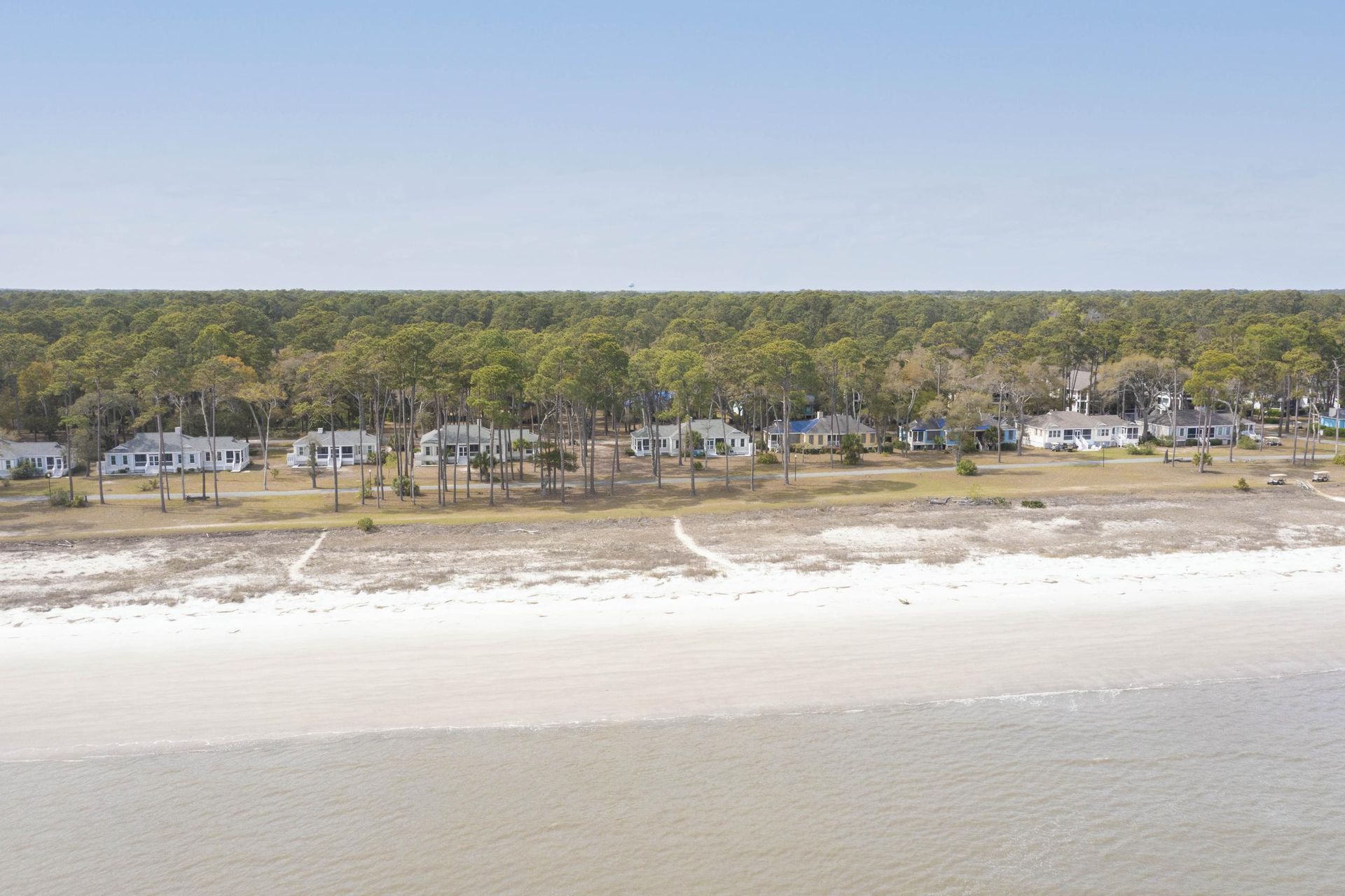 An aerial view of a beach with houses and trees in the background.