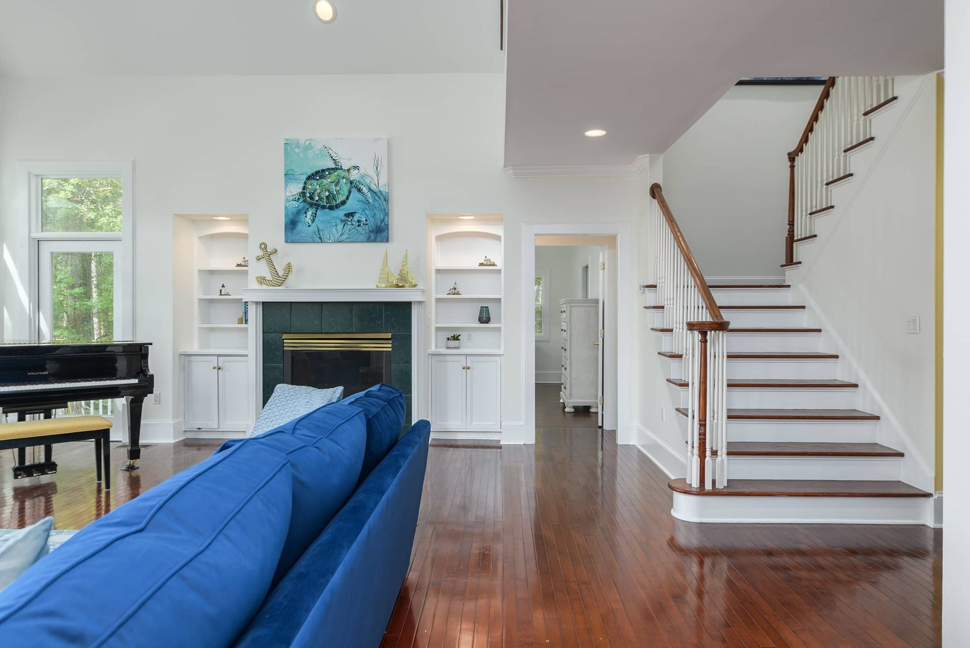 A living room with a blue couch , piano , fireplace and stairs.