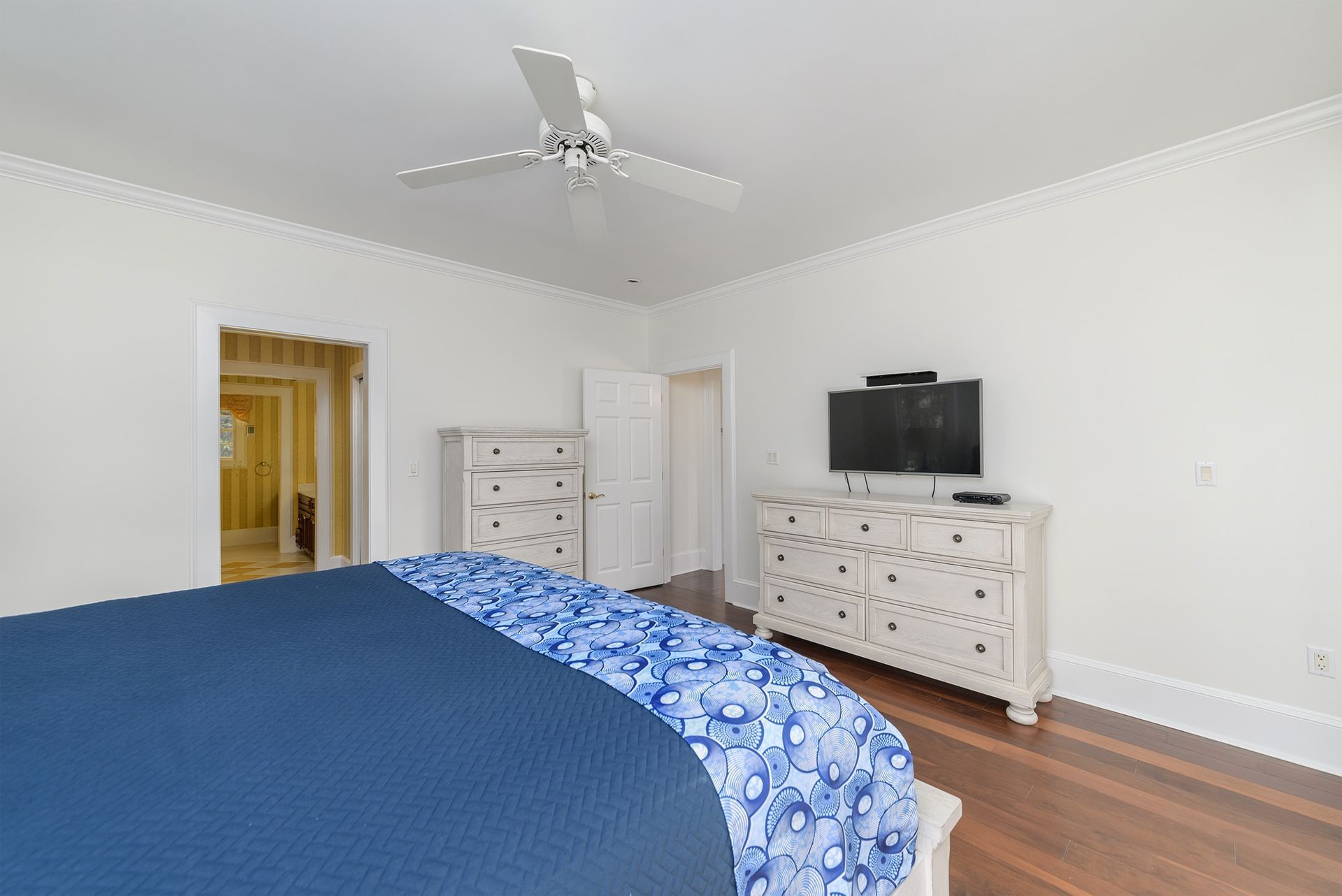 A bedroom with a bed , dresser , television and ceiling fan.