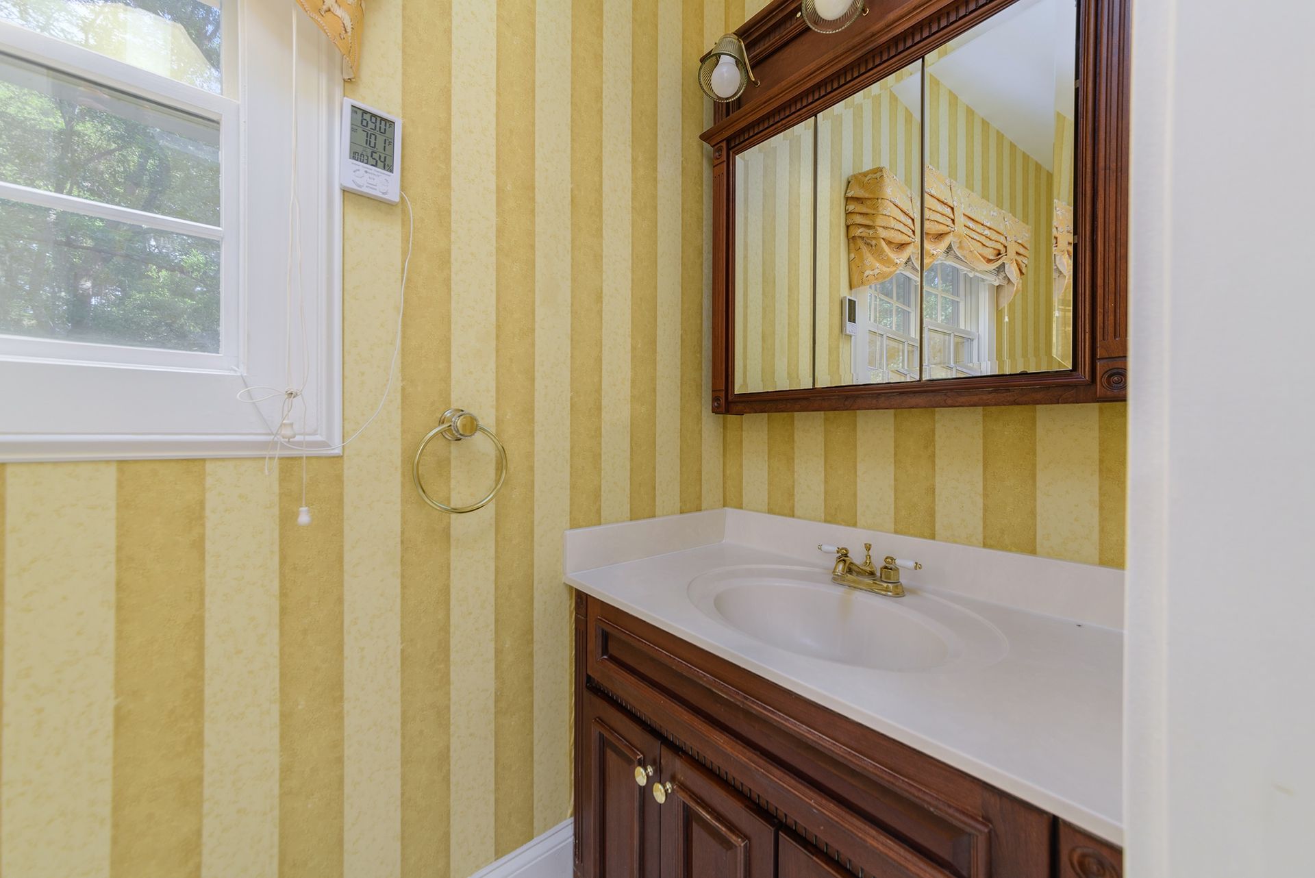 A bathroom with a sink , mirror and yellow striped wallpaper.