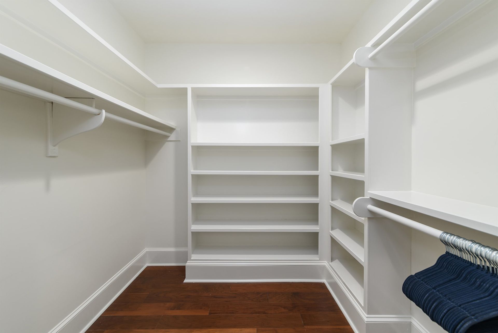 An empty walk in closet with white shelves and wooden floors.