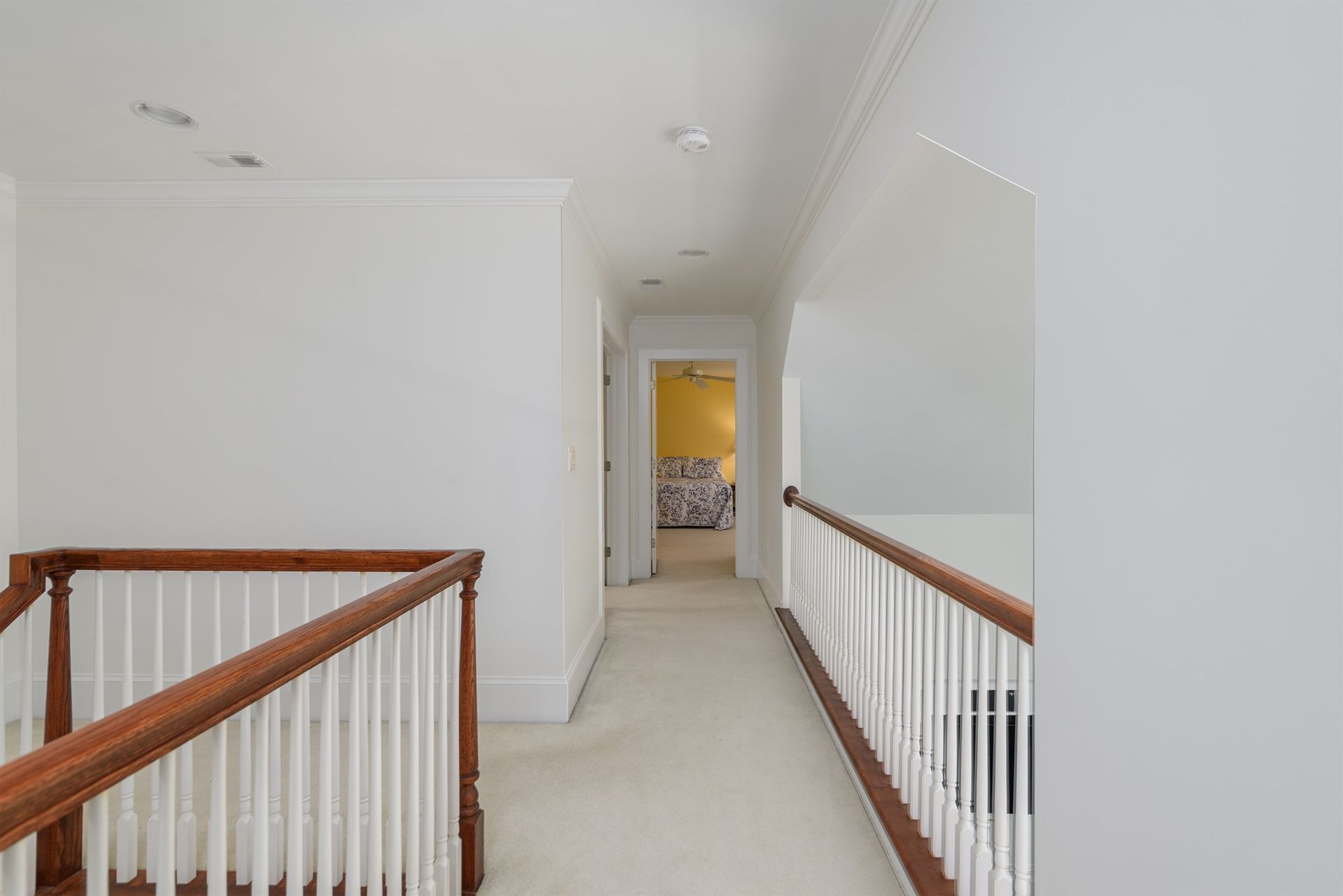 A hallway with a wooden railing and stairs leading to a bedroom.