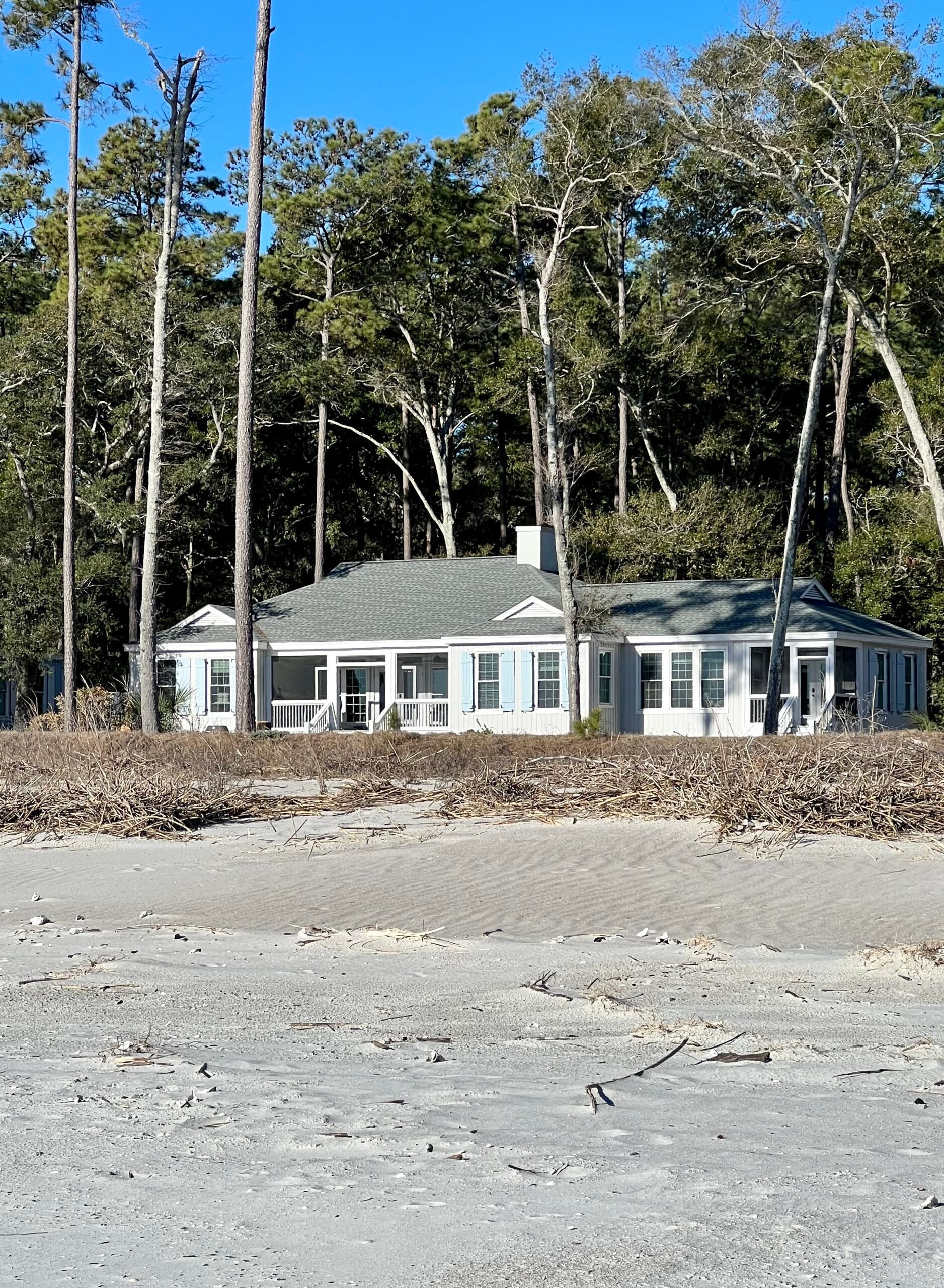 A white house sits on a sandy beach surrounded by trees
