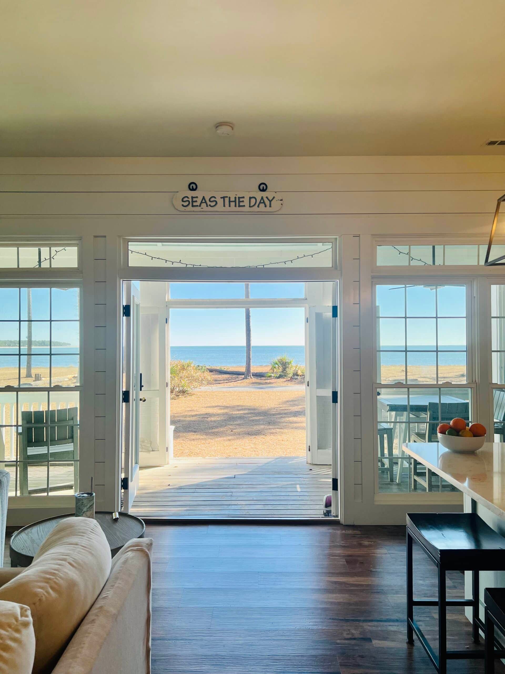 A living room with a view of the ocean and a sign that says seas the day.