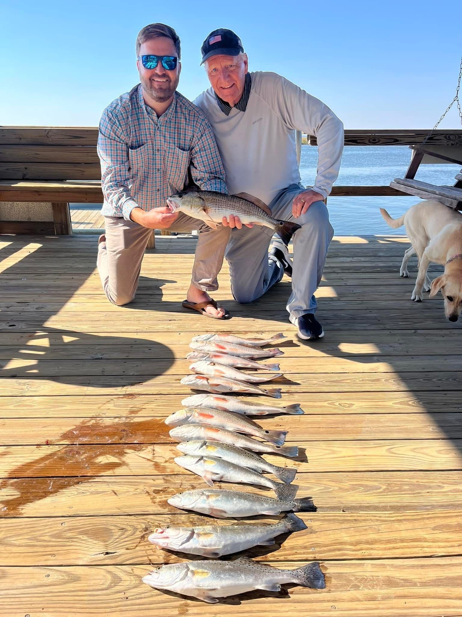 Two men are kneeling on a dock holding fish.