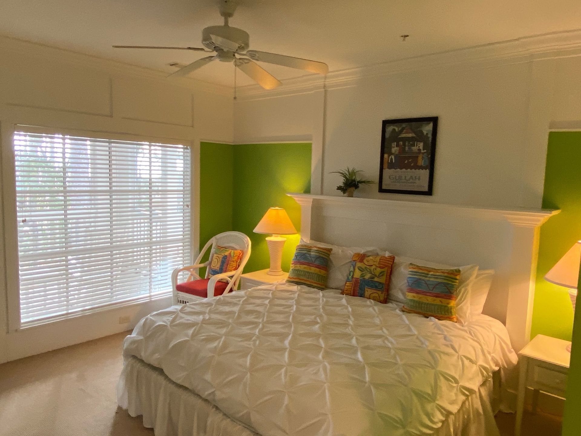 A bedroom with a bed , chair , lamps and a ceiling fan.