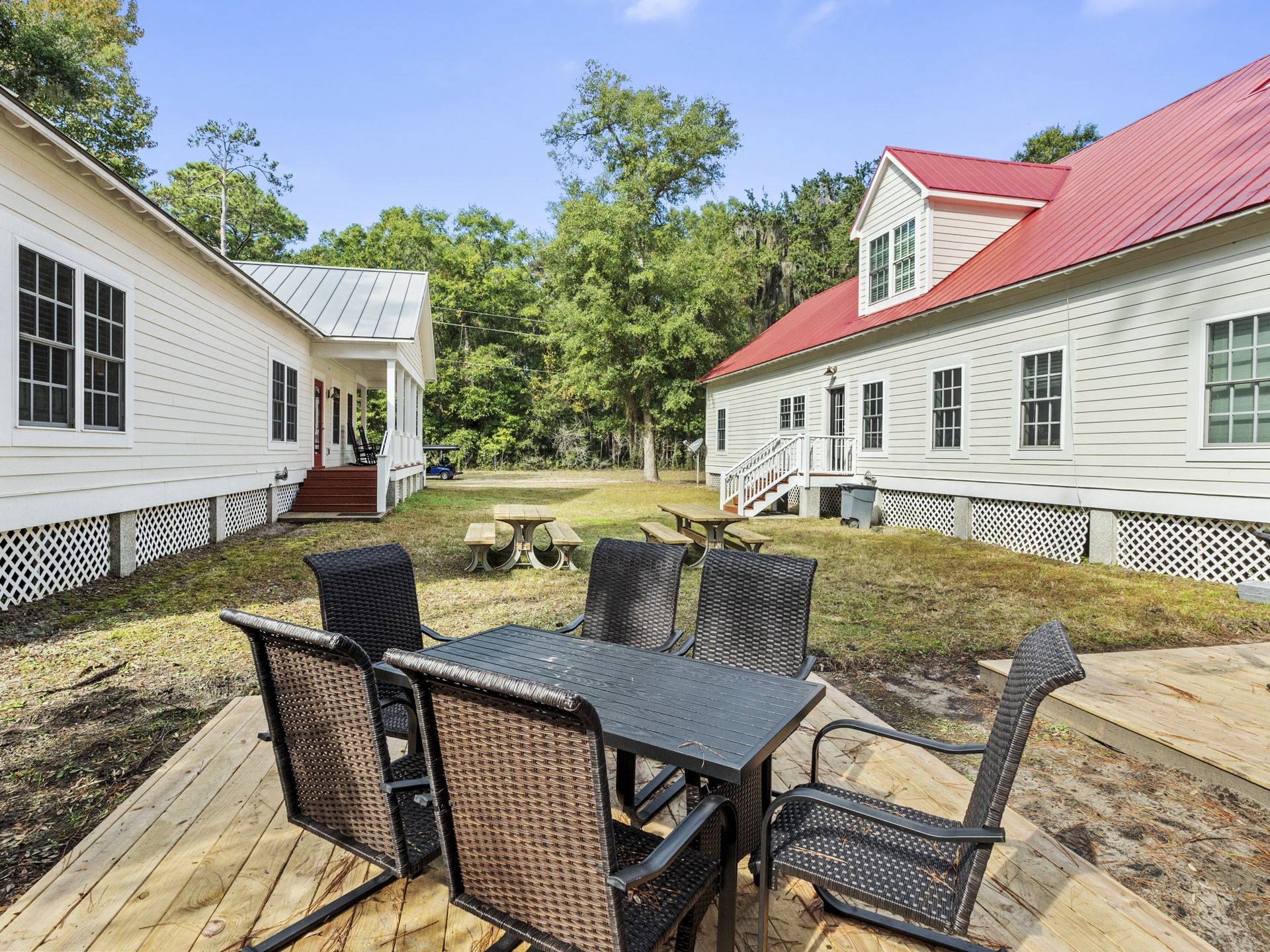 A patio with a table and chairs in front of a white house with a red roof.