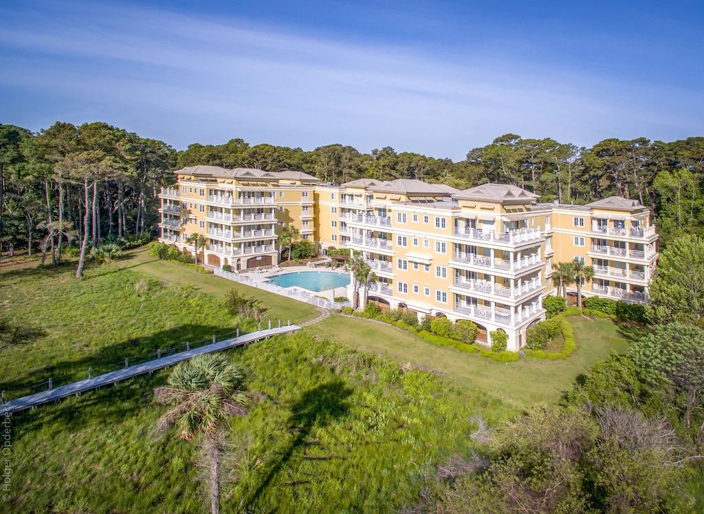 An aerial view of a large apartment building with a pool in the middle of a forest.