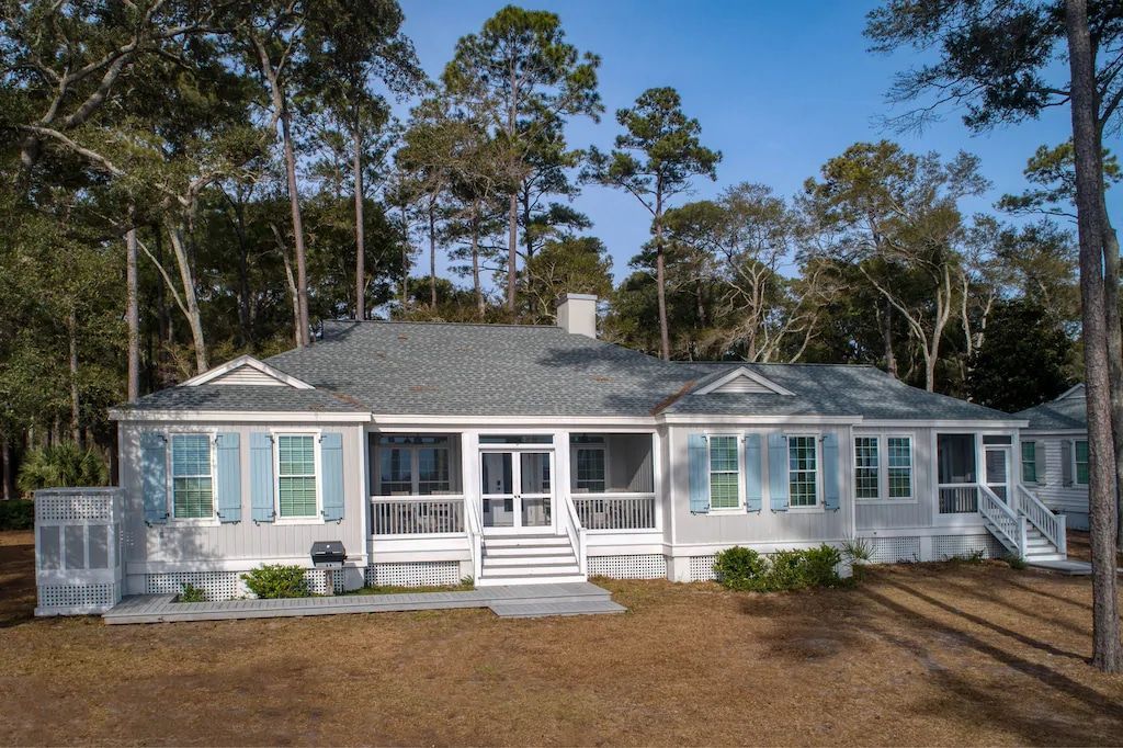 A large white house with a large porch is surrounded by trees.