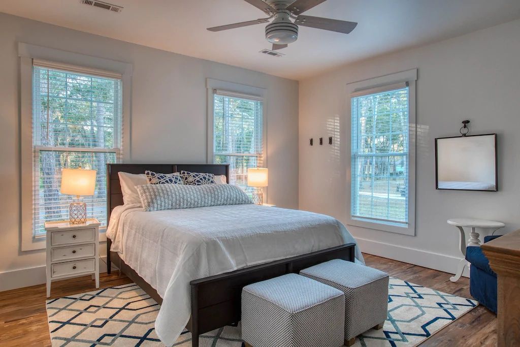 A bedroom with a bed , two ottomans , a ceiling fan and a television.