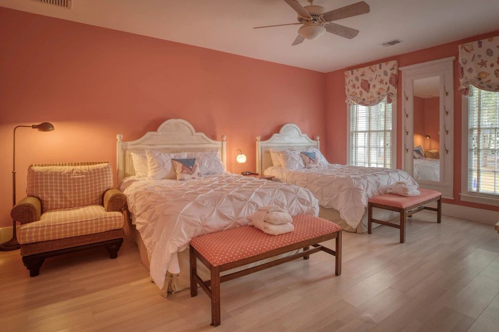 A bedroom with two beds , a bench , a chair and a ceiling fan.