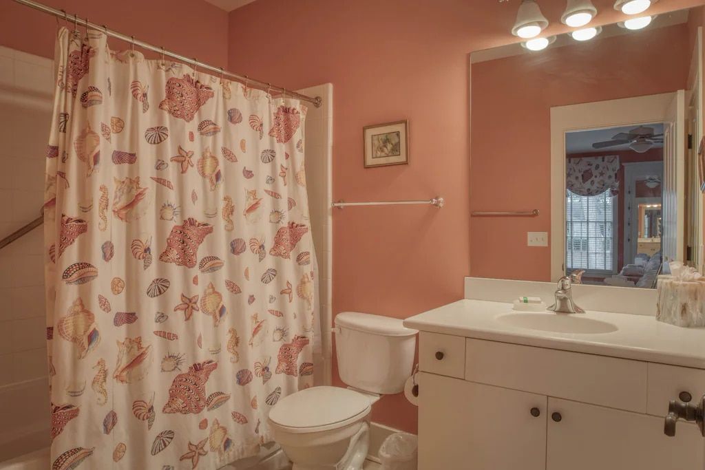 A bathroom with a toilet , sink , shower curtain and mirror.