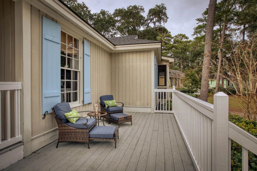 A deck with chairs and a table on it in front of a house.