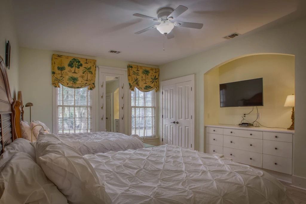 A bedroom with two beds , a television and a ceiling fan.