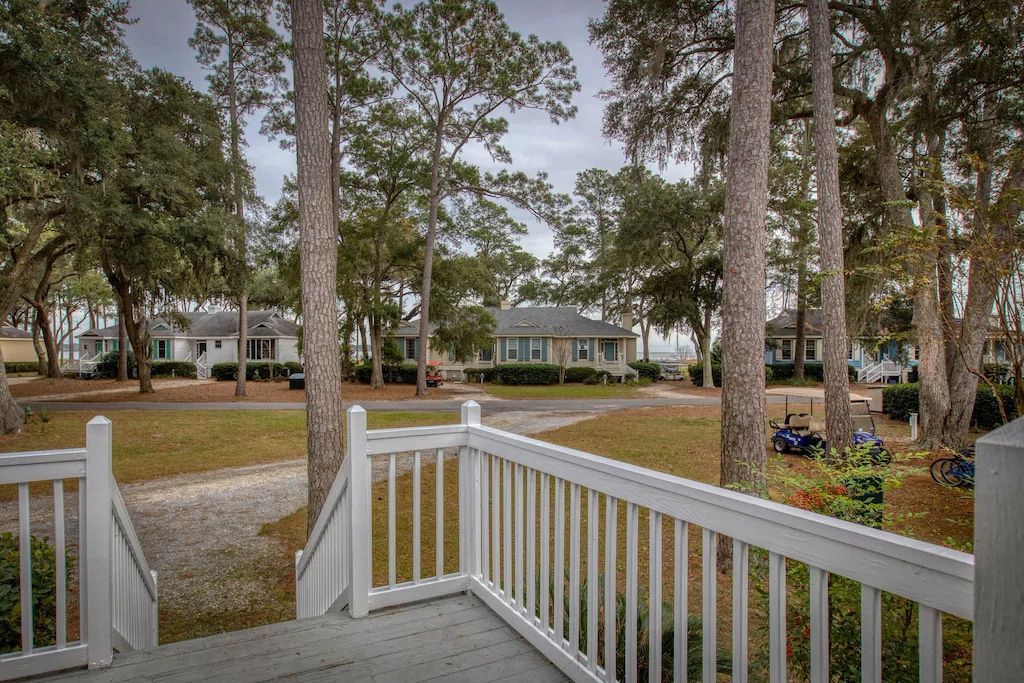 A deck with a white railing surrounded by trees and a house in the background.