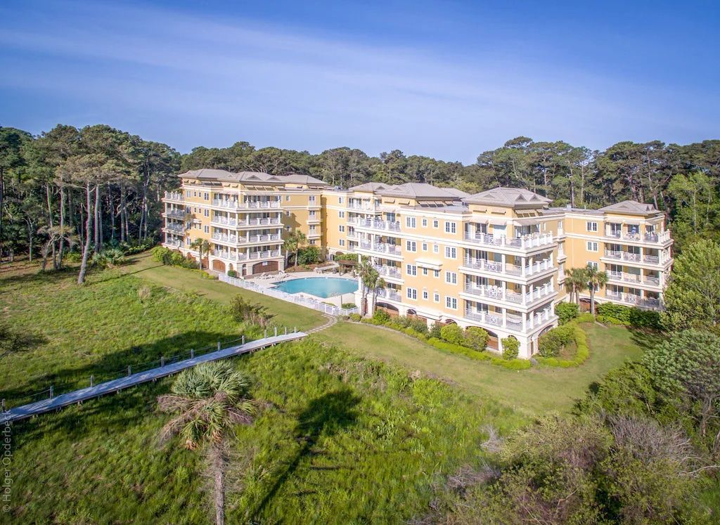 An aerial view of a large apartment building with a swimming pool surrounded by trees.
