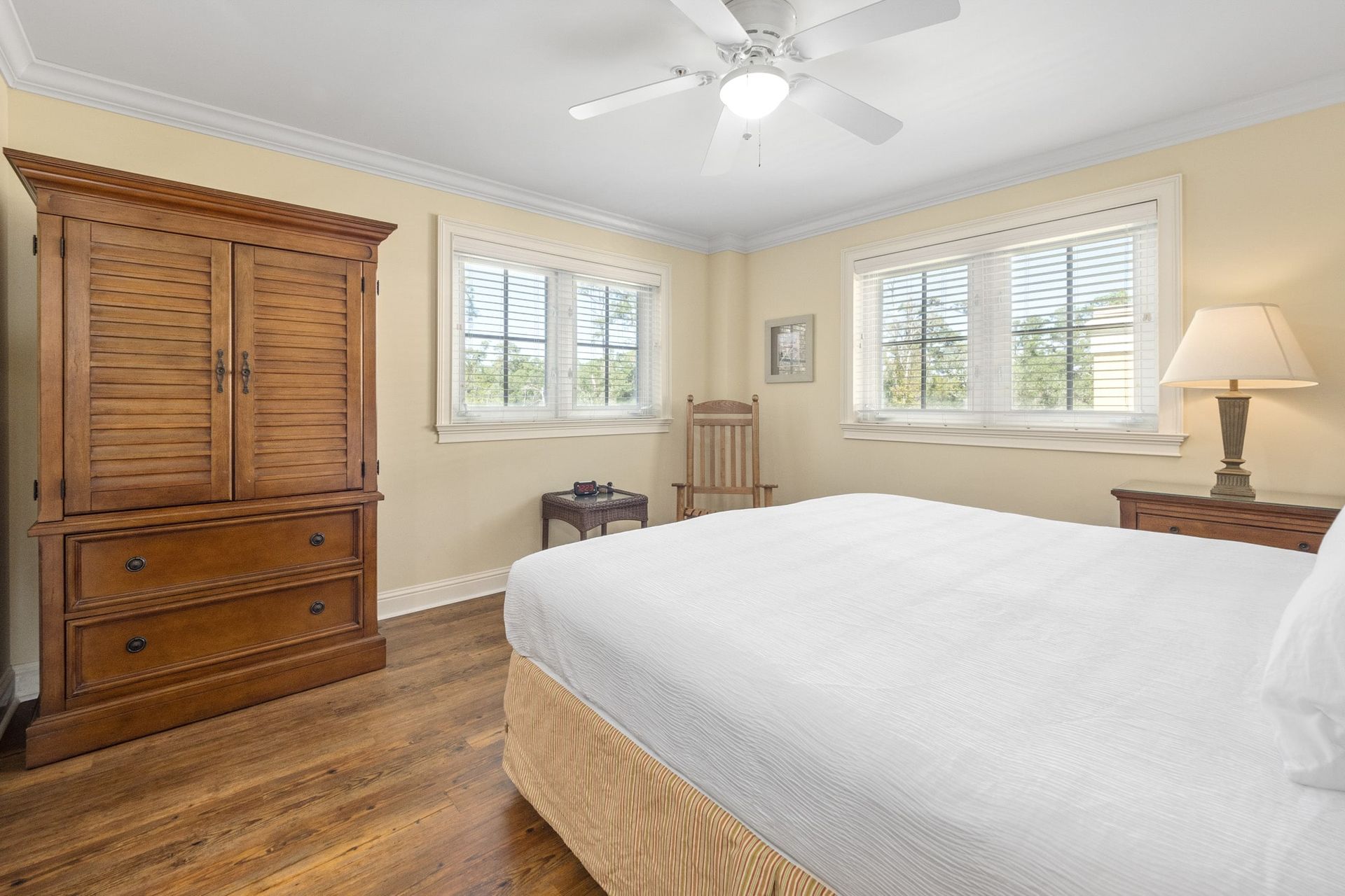 A bedroom with a bed , dresser , chair and ceiling fan.