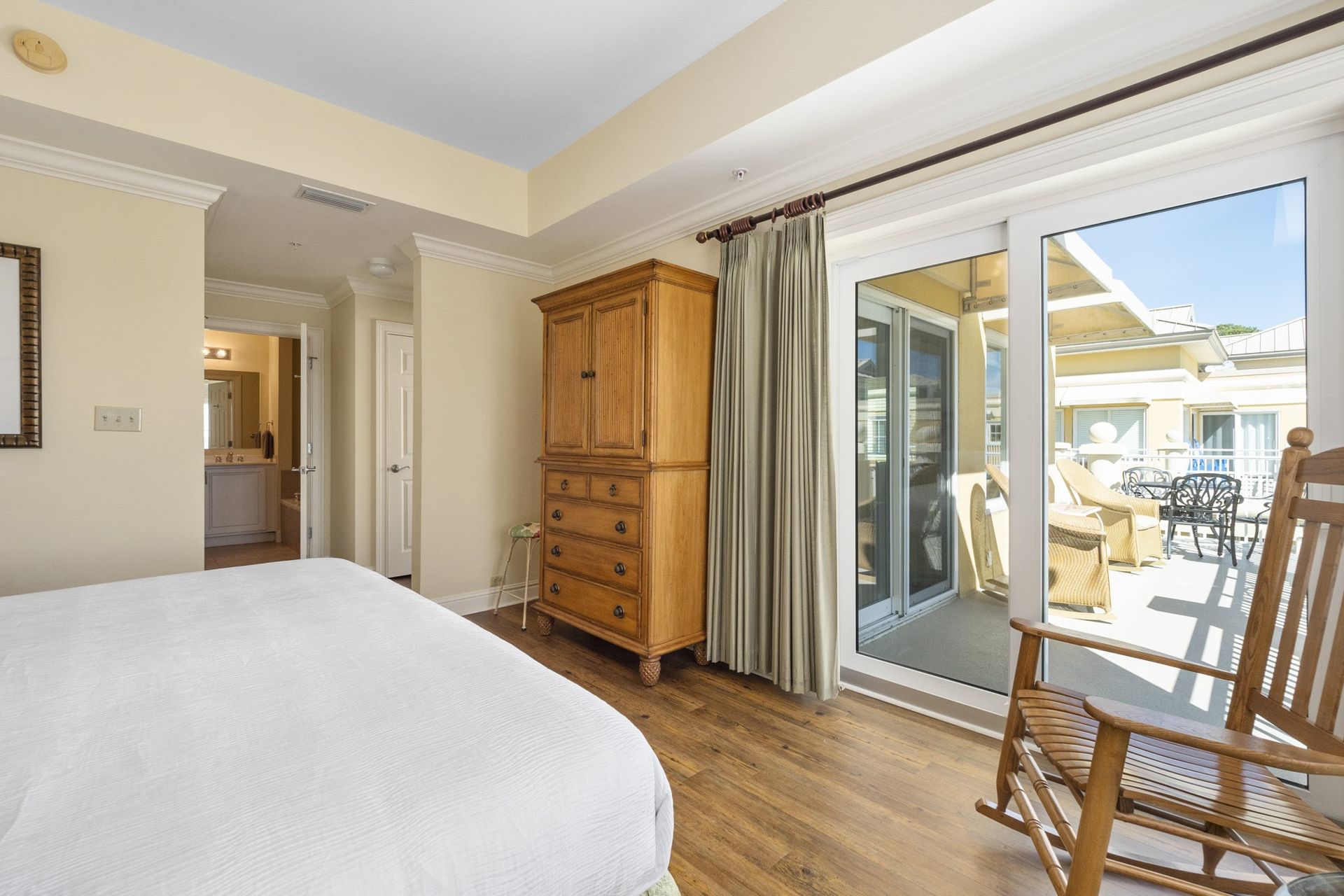 A bedroom with a bed , dresser , rocking chair and sliding glass doors leading to a balcony.