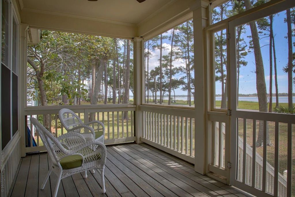 A screened in porch with a chair and table and trees in the background.
