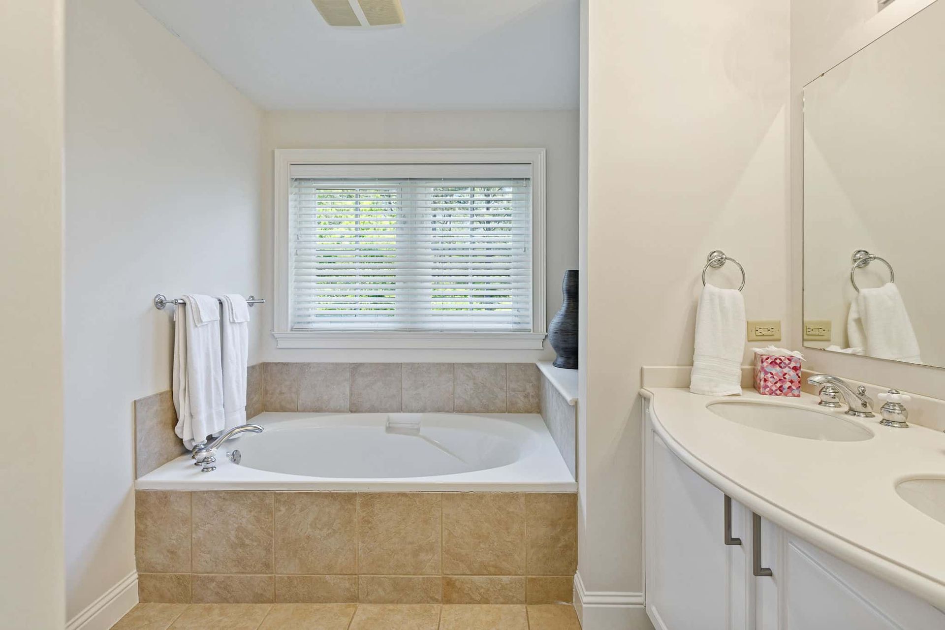 A bathroom with a tub , sink , mirror and window.