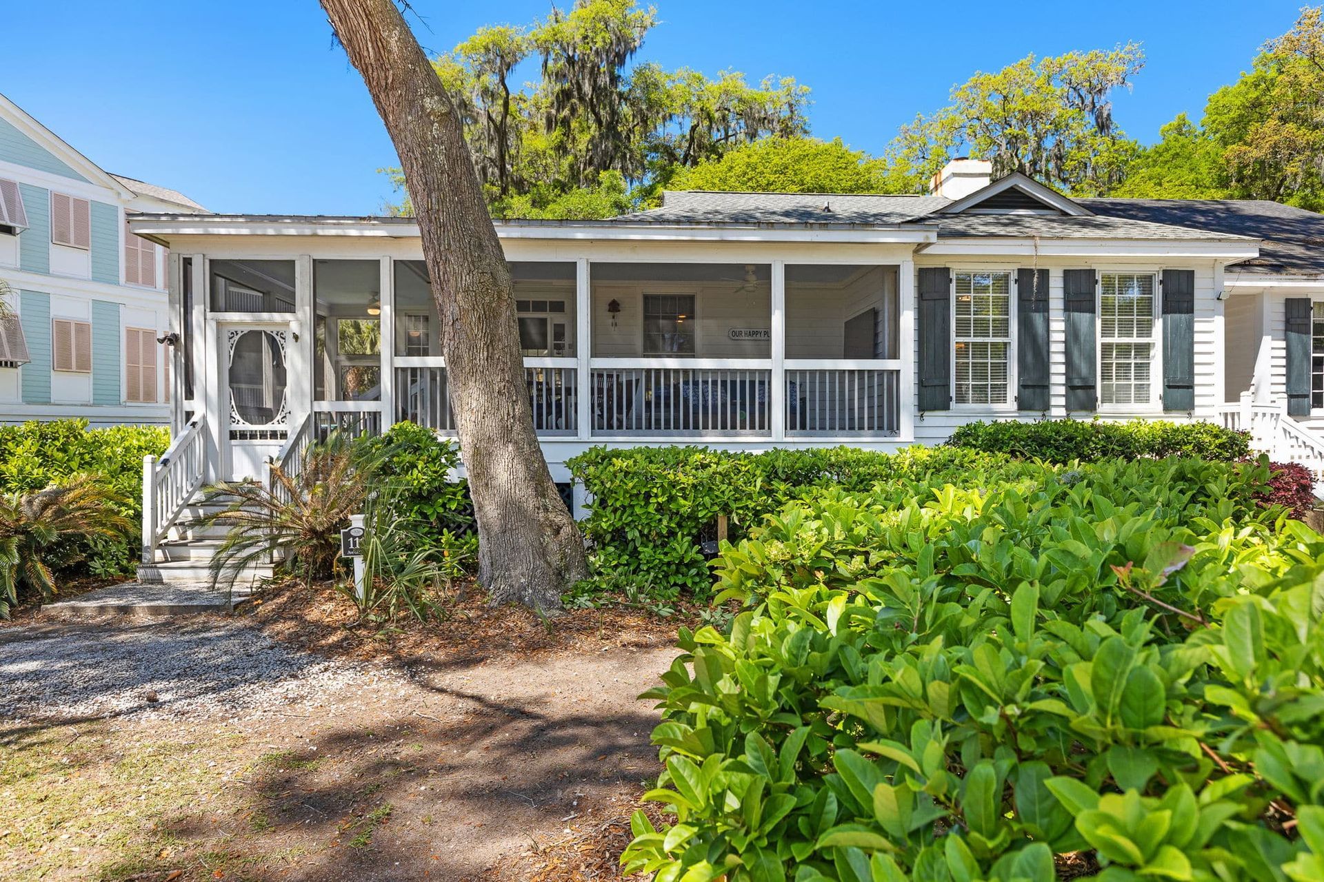 A white house with a screened in porch is surrounded by trees and bushes.
