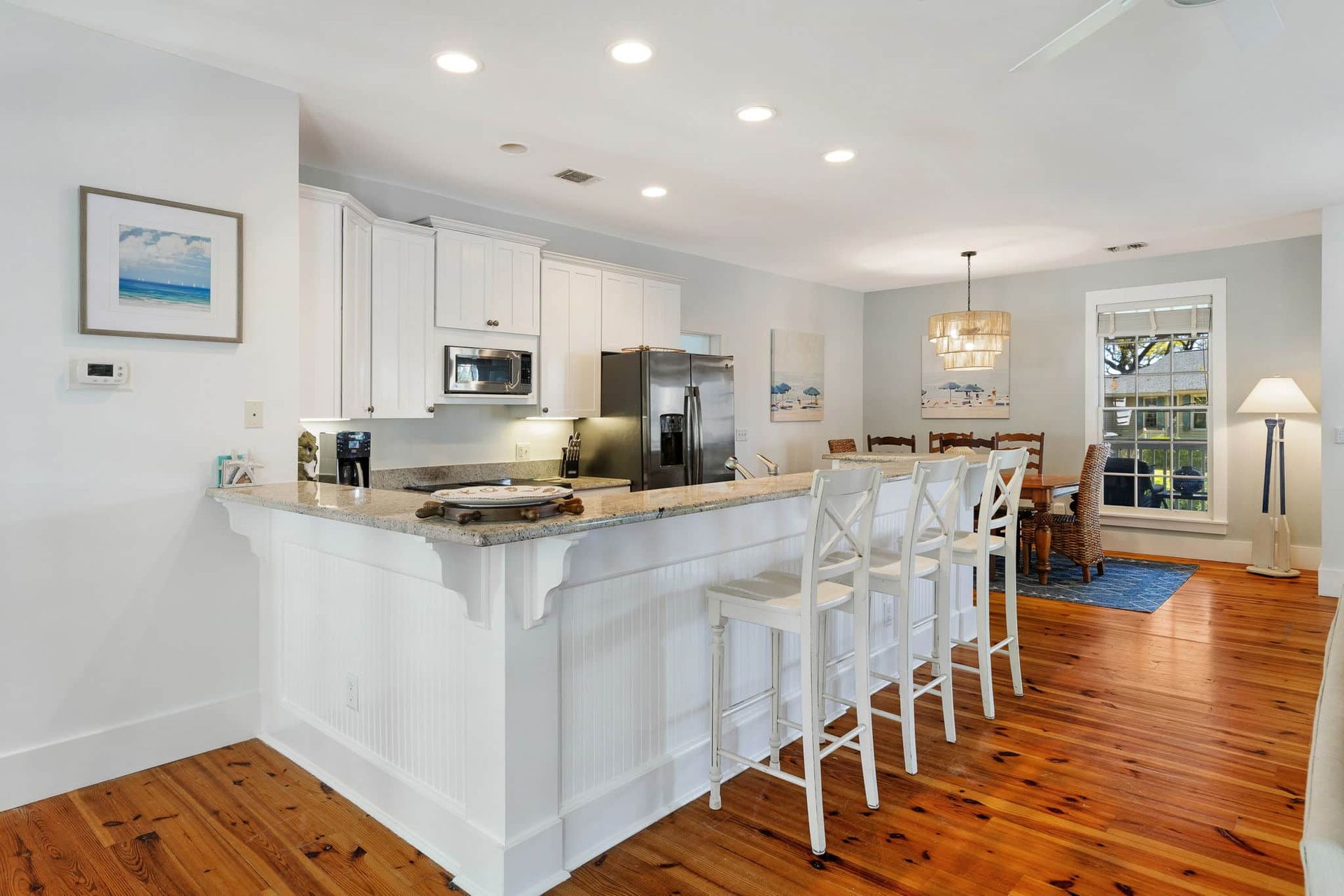 A kitchen with white cabinets , granite counter tops , stainless steel appliances and wooden floors.