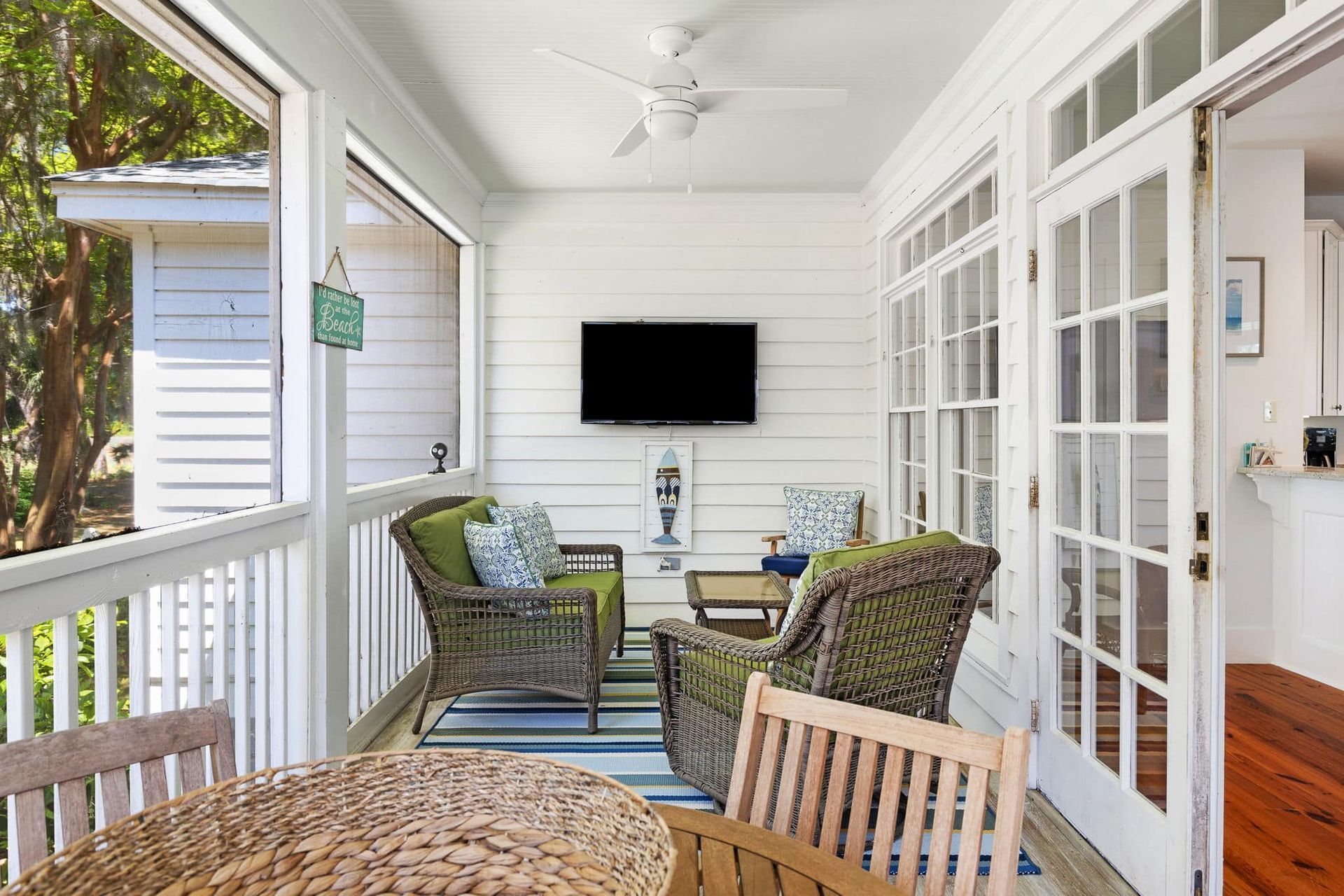 A porch with a table , chairs , a television and a ceiling fan.