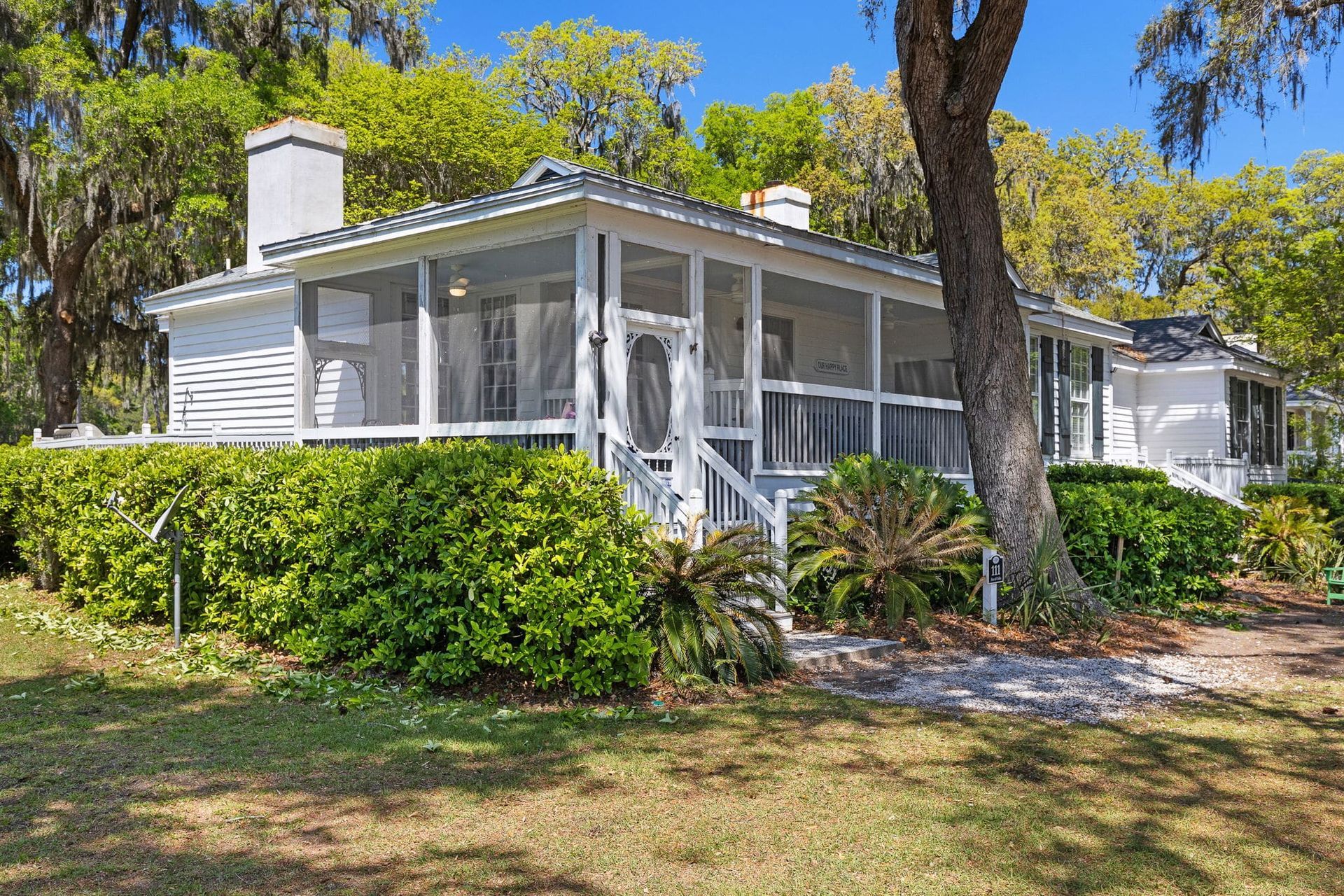 A white house with a screened in porch and a tree in front of it.