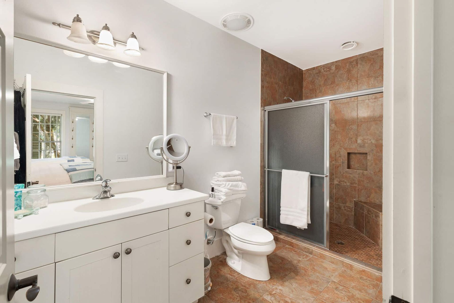 A bathroom with a toilet , sink , mirror and walk in shower.