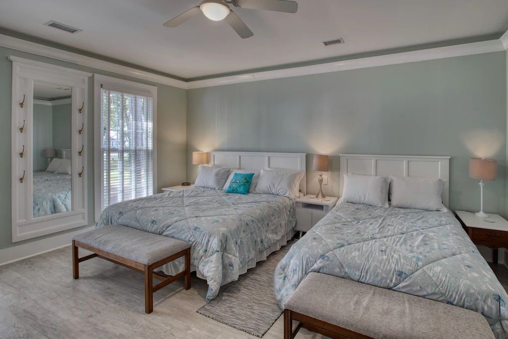 A bedroom with two beds , a bench and a ceiling fan.
