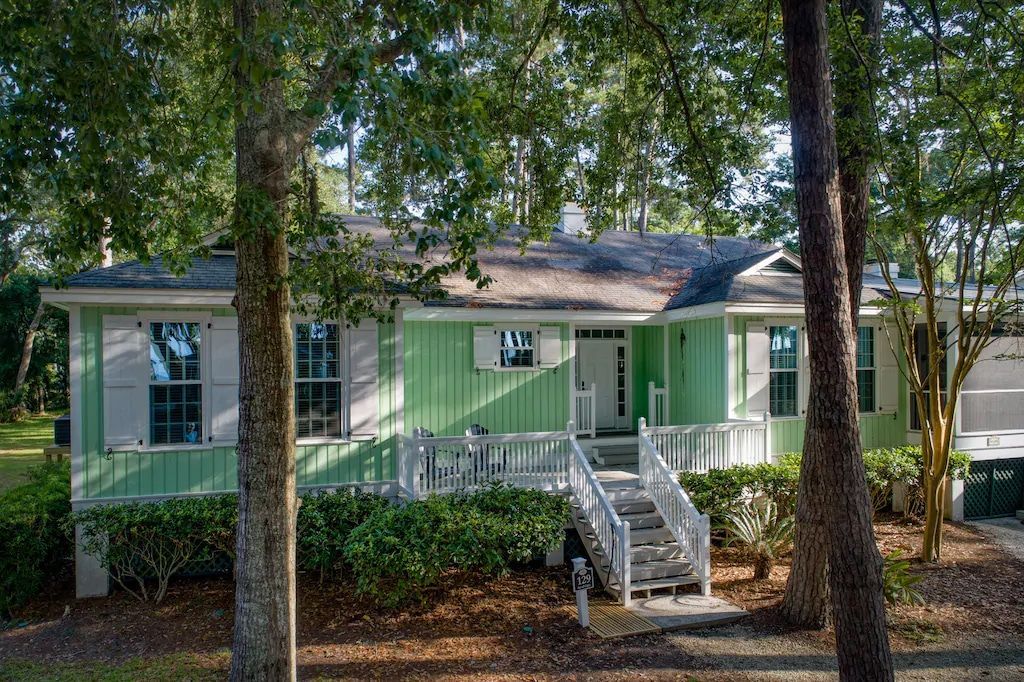 A green house with white shutters is surrounded by trees.