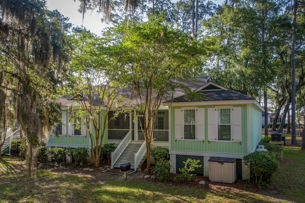 A green and white house is surrounded by trees and grass.
