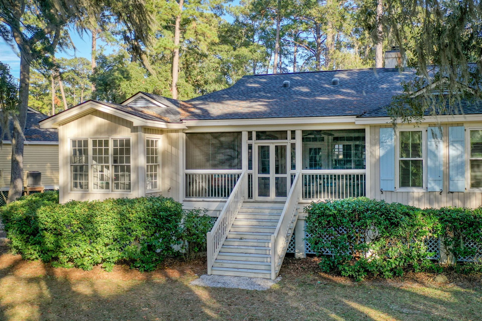 A house with a screened in porch and stairs is surrounded by trees.