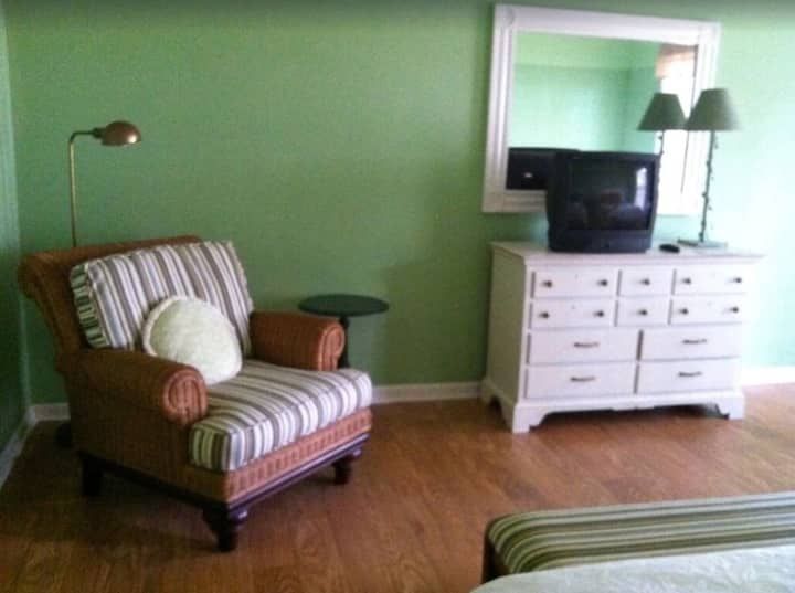 A bedroom with a chair a dresser and a television
