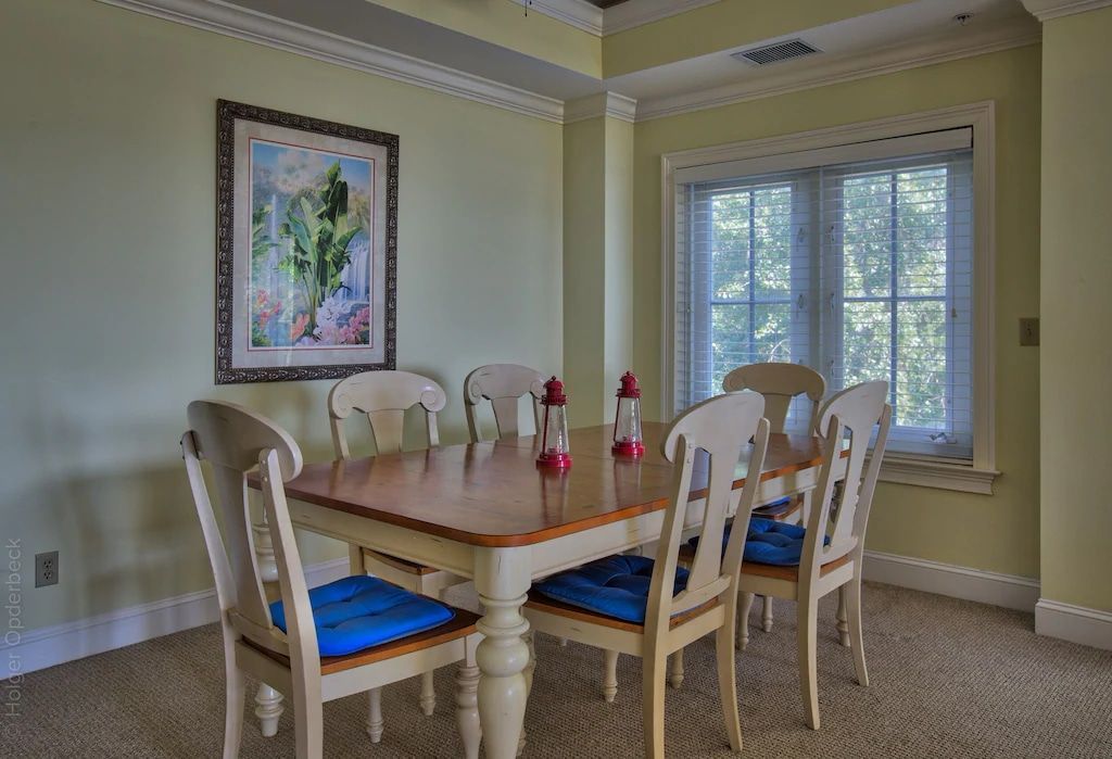 A dining room with a table and chairs and a painting on the wall.